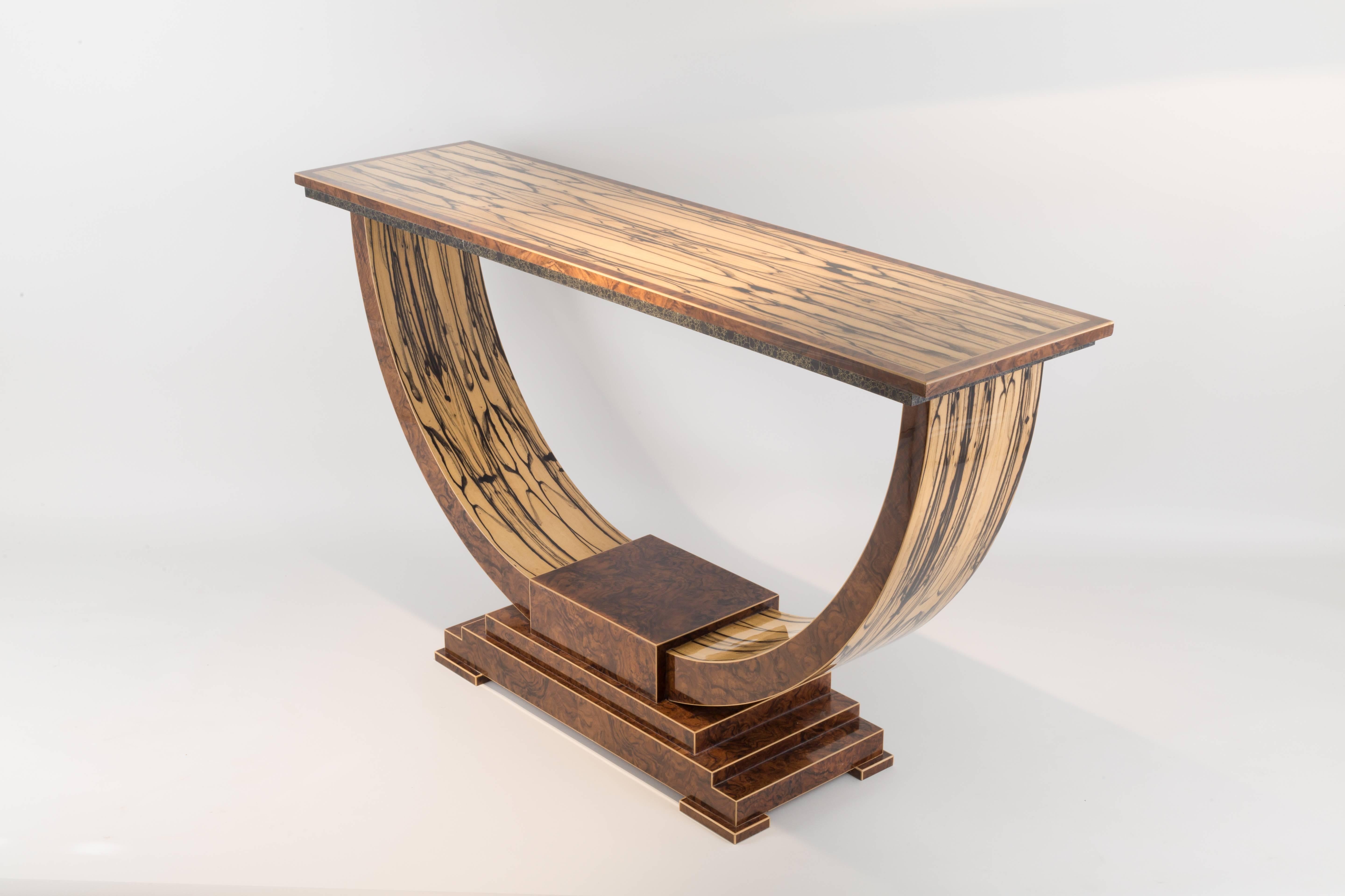 A rare and exquisite veneer, white ebony is used extensively throughout. Beautifully figured, it is paired with fine English walnut. The stone edging incorporating gold thread is produced especially for this table completing this refined console