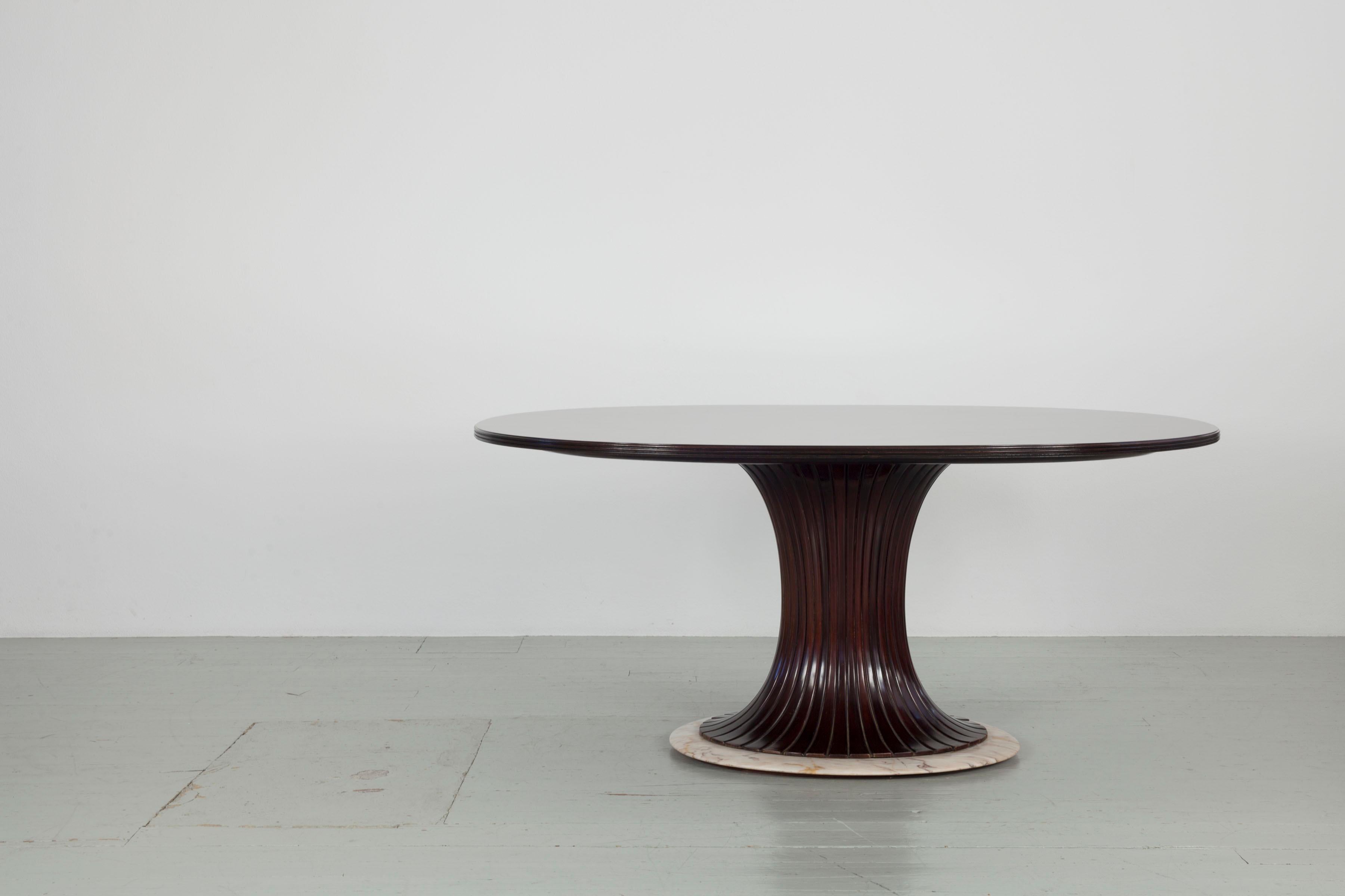This table in the style of Vittorio Dassi was designed in the 1950s. The oval tabletop made of rosewood veneer sits on an hourglass-shaped central leg made of dark brown stained wood. The entire table is attached to a pink marble base, which creates