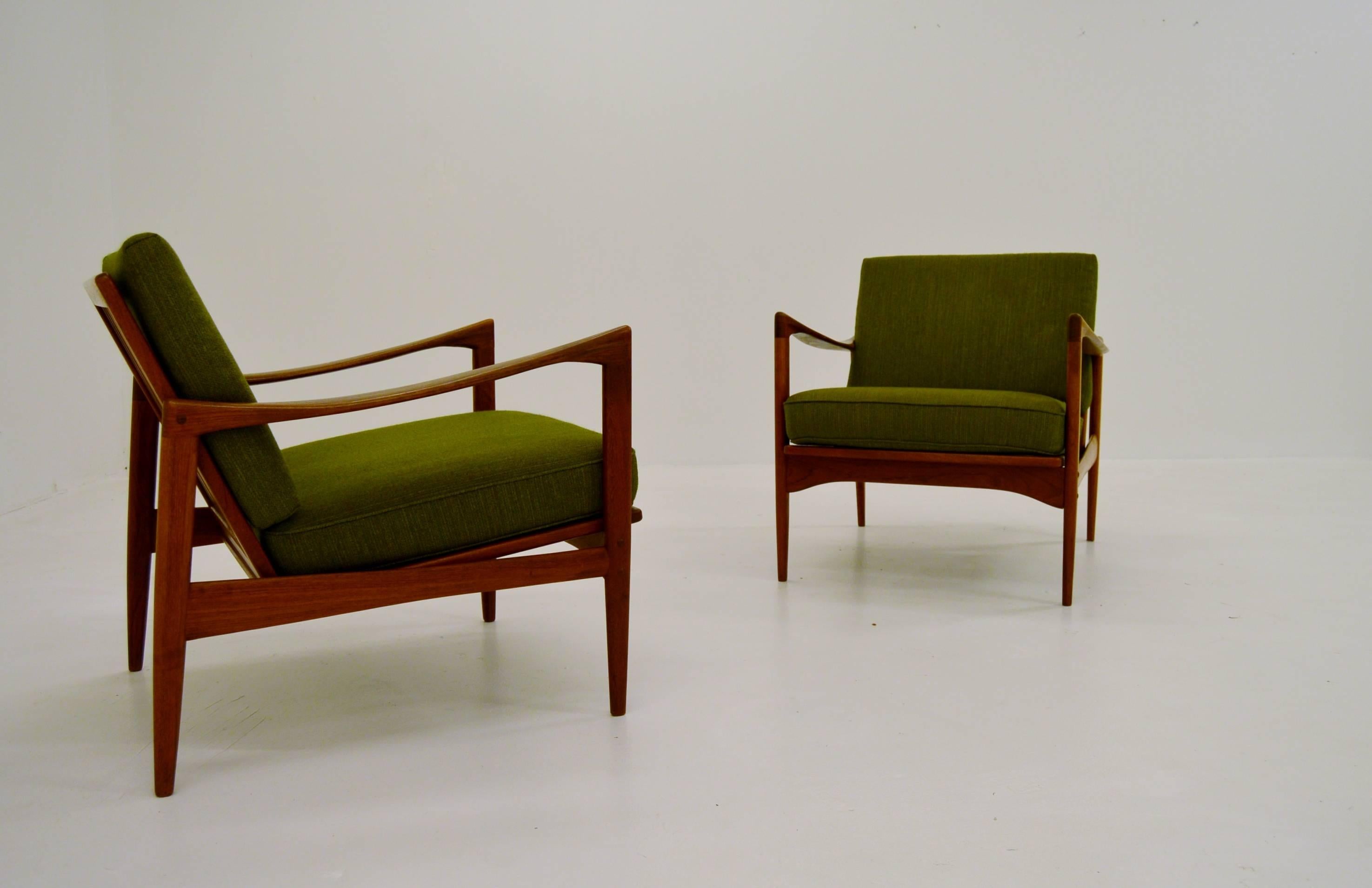 Elegant pair of Ib Kofod Larsens comfortable lounge chairs "Kandidaten". Made from solid teak.

These armchairs have just got a new padding in the cushions by a professional upholsterer. The original fabric is intact with minor wear.
 