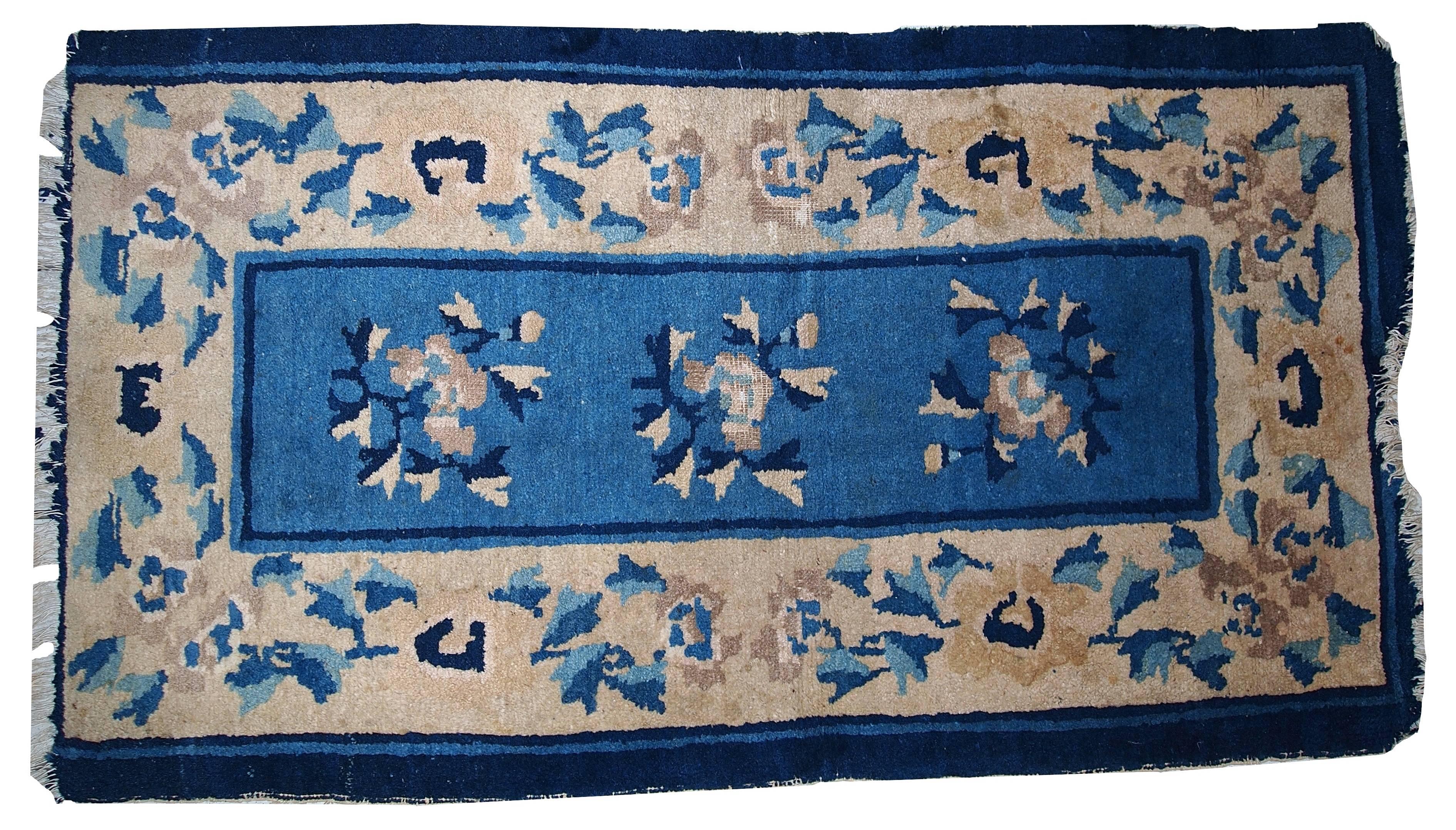 Antiker chinesischer Peking-Teppich in abgenutztem Zustand. Die erste Bordüre ist marineblau, die zweite ist größer und beige und mit Blumen bedeckt. Der mittlere Bereich ist blau und hat drei ähnliche Blumen. Bei diesem Teppich fehlt eine Bordüre