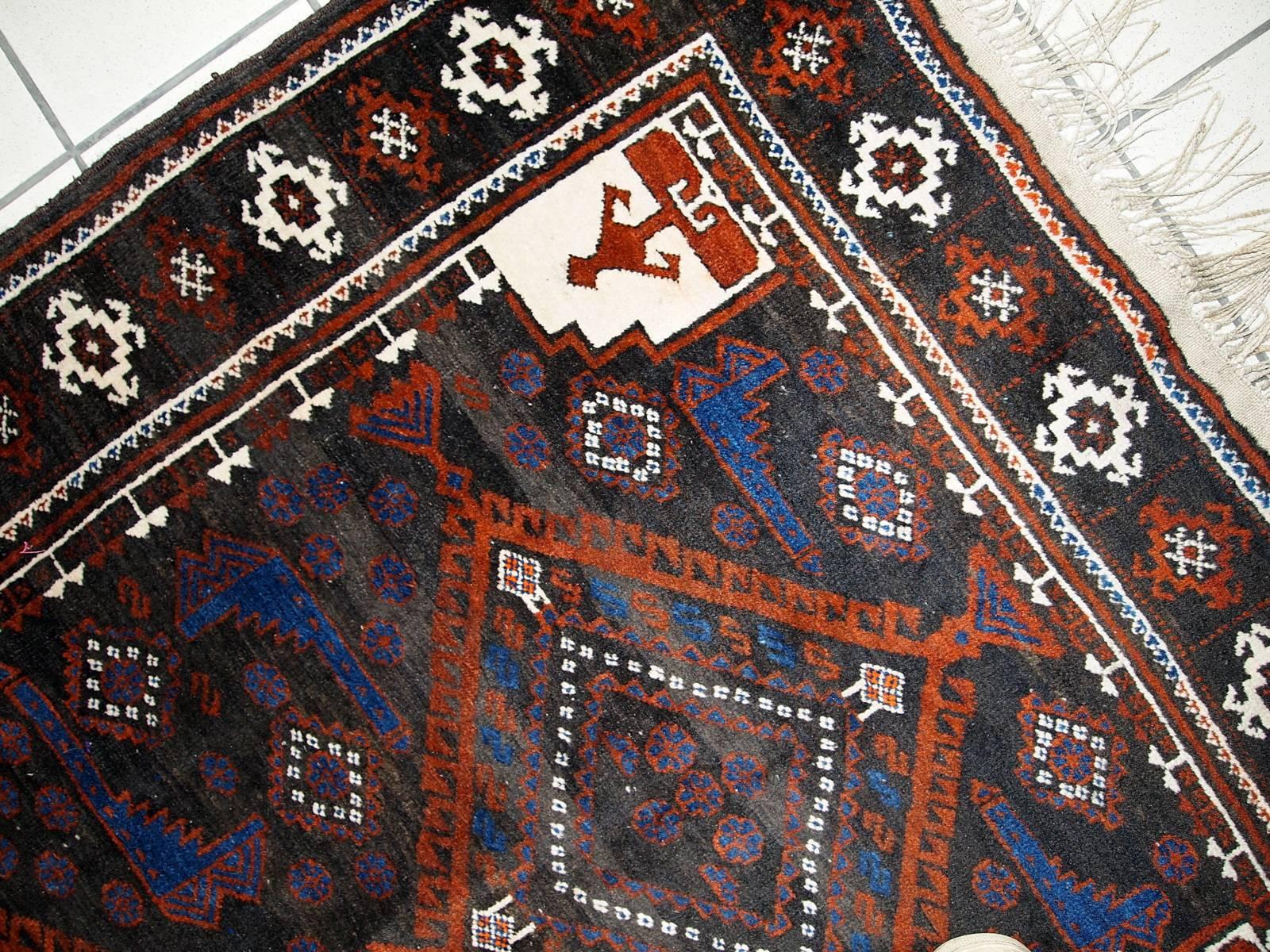 Vintage handmade Afghan Baluch rug. Rusty red, bright blue and white tribal figures are spread around chocolate brown field of this rug. The rug is vintage and it's style represents Afghan culture of 1930s. The rug is quite dark, so will be perfect
