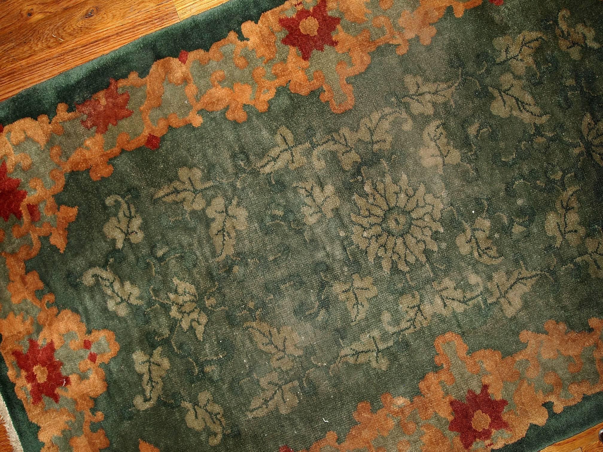 Art Deco Chinese rug in green shade. Thick orange border with a bright red flowers in the middle of it. Filed is in green color and has very light beige shadows of falling foliage's all around it. Beautiful carpet for your home.