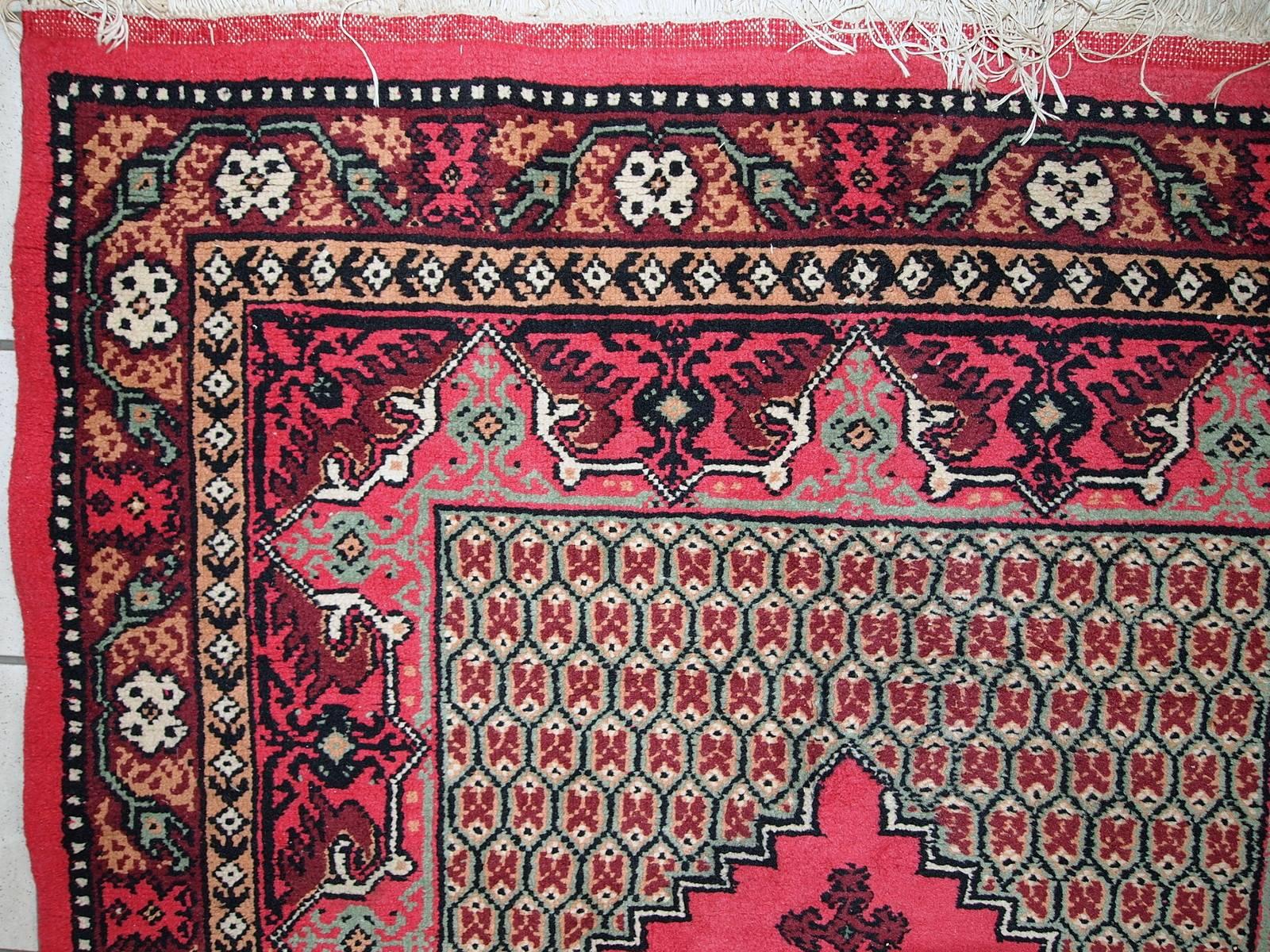 Algerischer Berberteppich im Originalzustand. Der Teppich hat ein traditionelles Berberdesign mit einem großen rautenförmigen Medaillon in der Mitte in rosa Farbe. Die tief burgunderrote Bordüre ist mit floralen Ornamenten verziert. Der Teppich ist