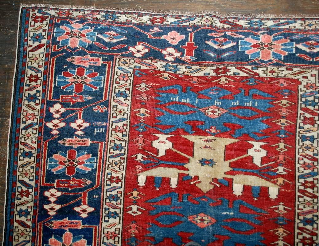 Antique handmade Caucasian Shirvan rug in good condition. This rug has been made in Azerbaijan. Very interesting narrow central area made in bright red shade. The tribal design in orange, beige and blue decorating it. The wide navy blue border