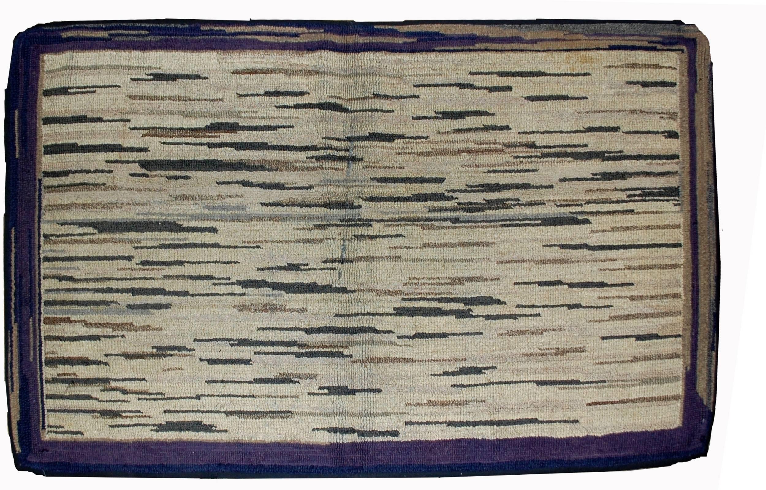 Handgefertigter antiker amerikanischer Hakenteppich in gutem Zustand. Der Teppich hat ein für die damalige Zeit modernes Design. Bunte Streifen auf dem beigen Schirm, umgeben von einem lila Rand. Der Teppich ist in einem guten Originalzustand.
   