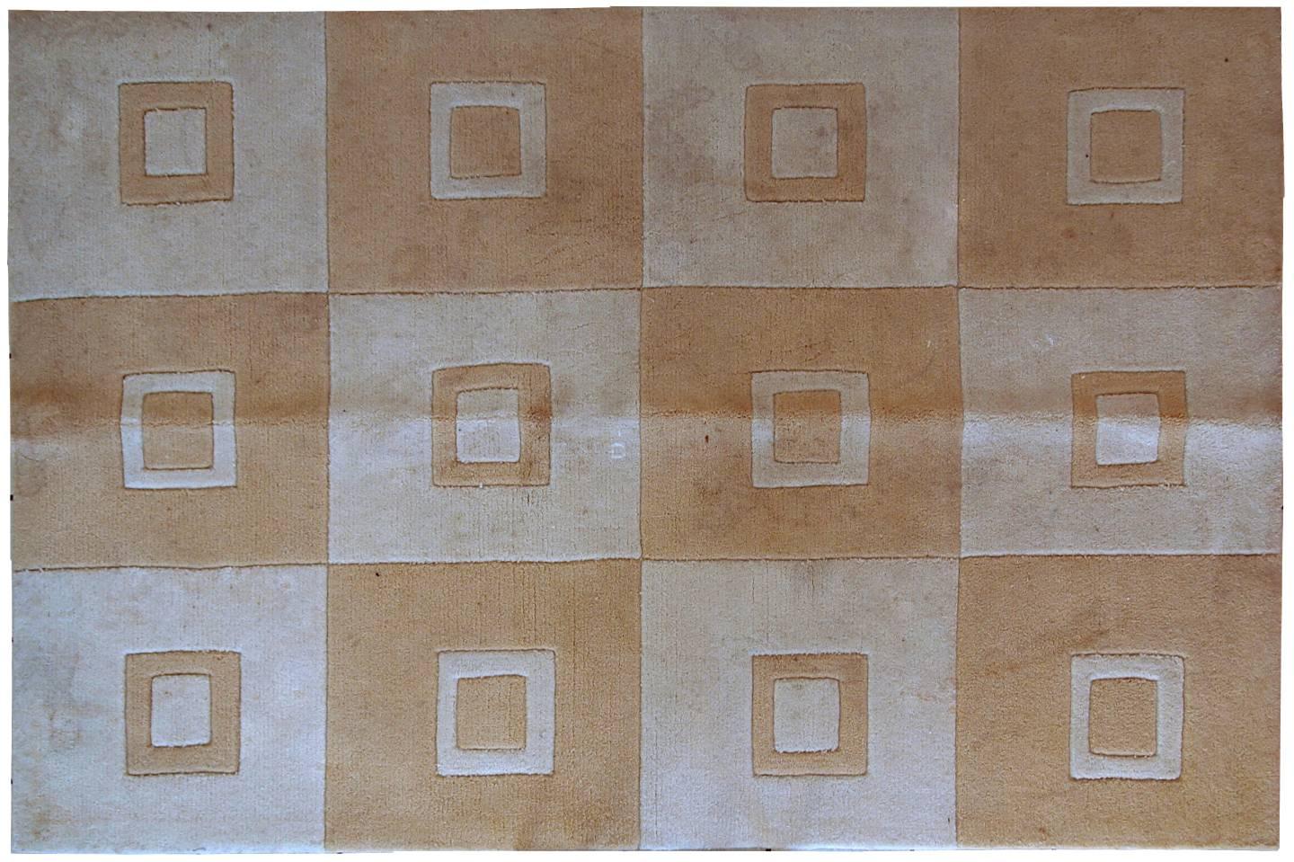 Alfombra china hecha a mano en tonos claros de blanco y marrón. Tiene un diseño geométrico moderno que contiene cuadrados. La alfombra se fabricó con acrílico en China. Está en estado original, tiene algunas decoloraciones propias de la edad.
 