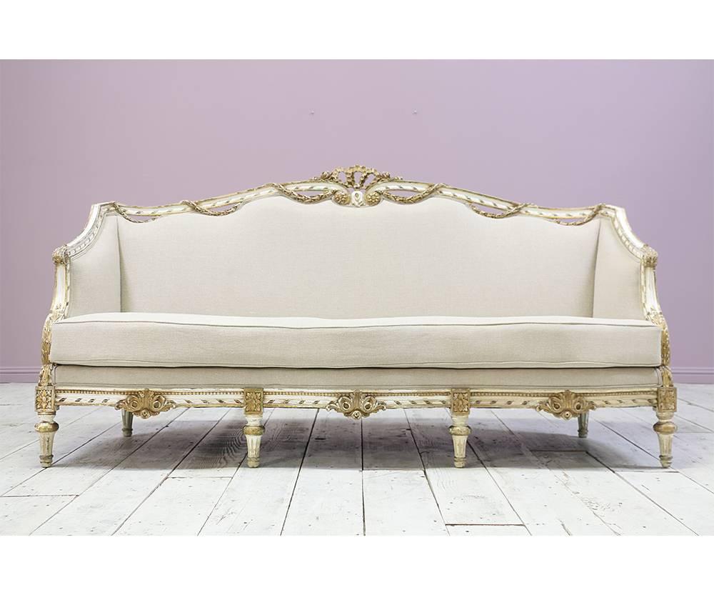 Gorgeous Italian, 1940s painted and parcel gilt carved wood sofa in the Louis XVI style. The sofa features beautiful carved decorations including a garland of laurel leaves, medallions, and a bow at its centre. Minor wood loss. Paint finish is