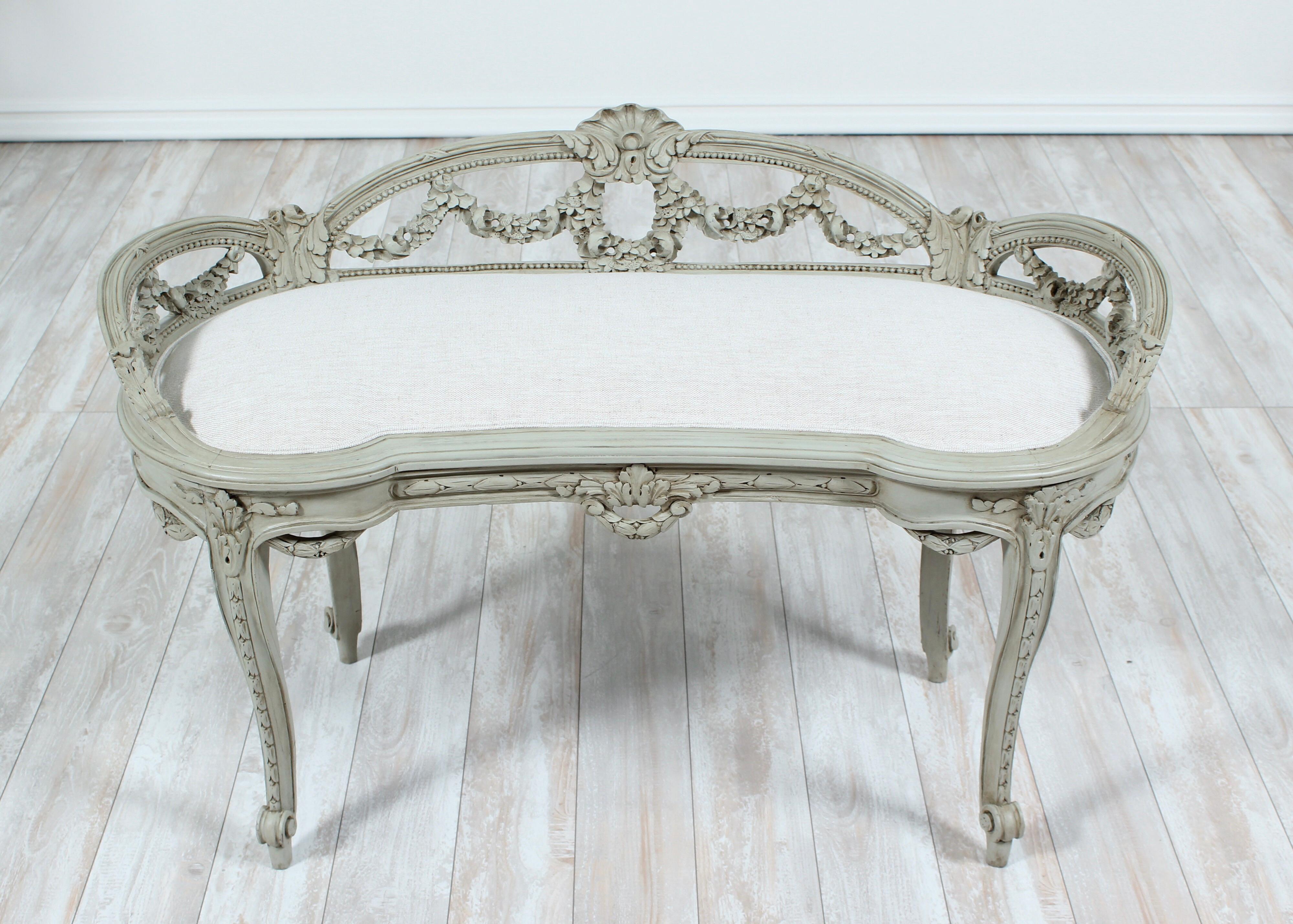 Beautiful French, 1920s Louis XV-style painted and carved wood bench with newly upholstered Belgian linen seat. The bench features delicately carved floral garlands, bead trim and cabriolet legs. Grey painted finish is naturally distressed. Seat