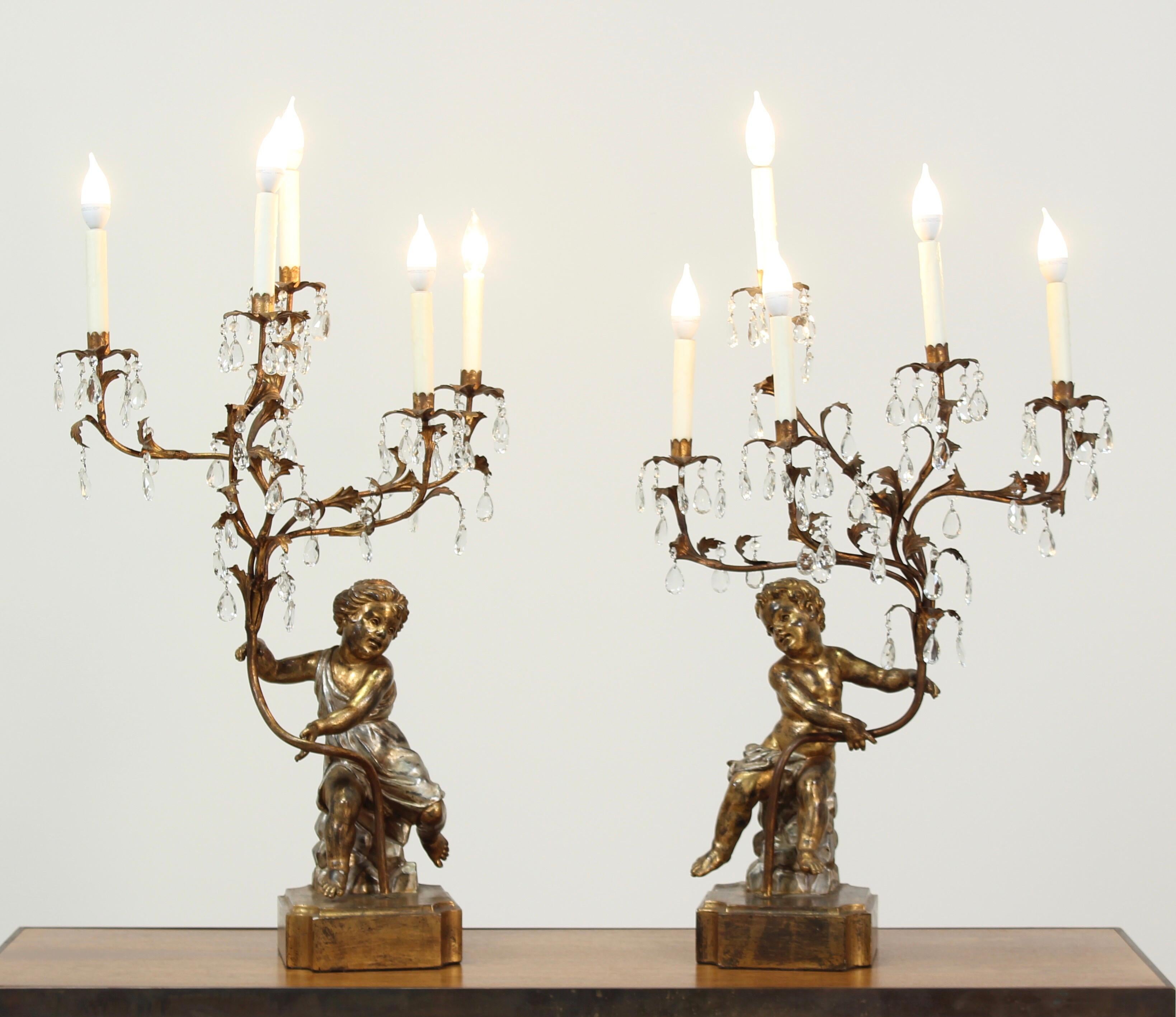 Wonderful pair of Italian silver-gilt carved wood candelabras depicting cherubs (one boy, one girl) holding iron branches. Each branch is decorated with crystal prisms and five candelabra lights (with new bee wax candle sleeves).