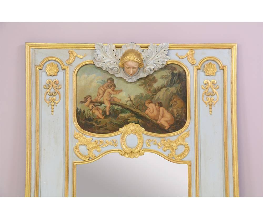 Monumental and impressive French, 1920s Louis XVI-style painted and parcel-gilt Trumeau mirror. This dramatic mirror features a grayish-blue paint finish with finely carved gilt accents and the carved face of an angel which is mounted above an oil