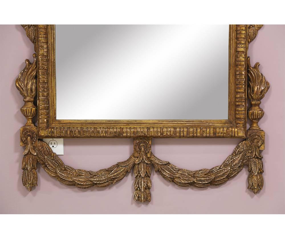  Impressive pair of carved gilt wood mirrors in the Neoclassical style. These beautiful large-scale mirrors feature nicely carved solid wood frames with a distressed gilt finish. Minor silver loss to one mirror plate which is consistent with age.