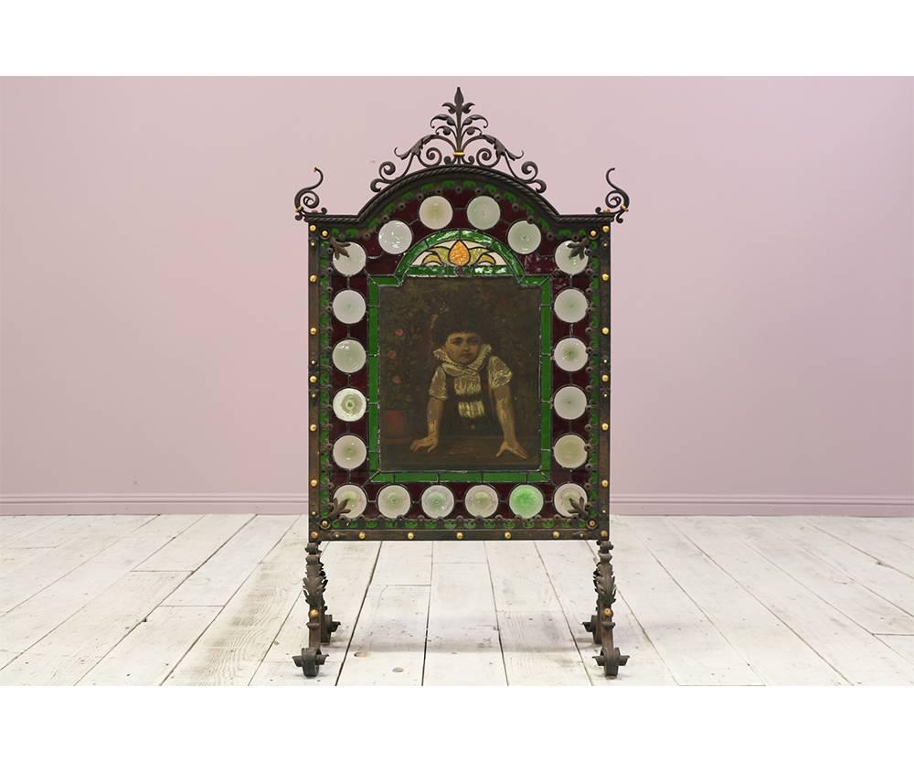 Exceptional antique French late 19th century intricately forged wrought iron fire screen with beautiful stained glass inserts and a delicate painting of a small child in the center. The purpose of this piece is to serve as a fire place screen but