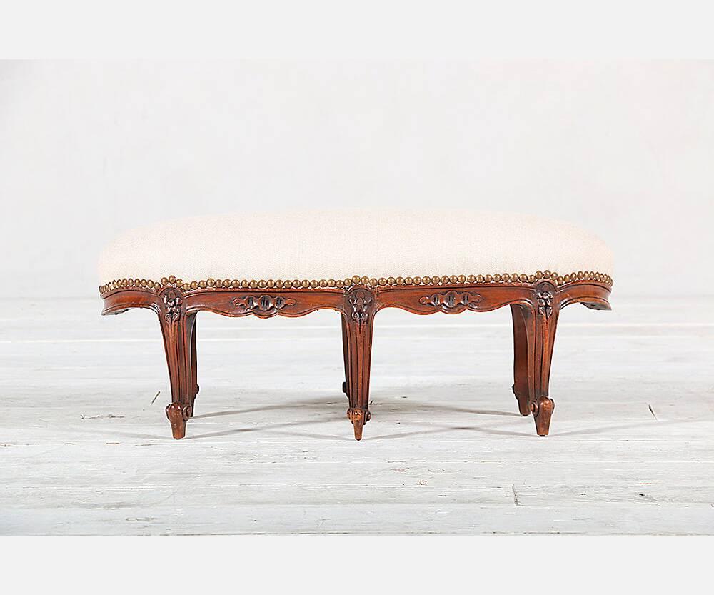 French, Louis XV-style footstool featuring six delicately carved cabriole legs and new linen upholstery with brass nail-head trim detail.
