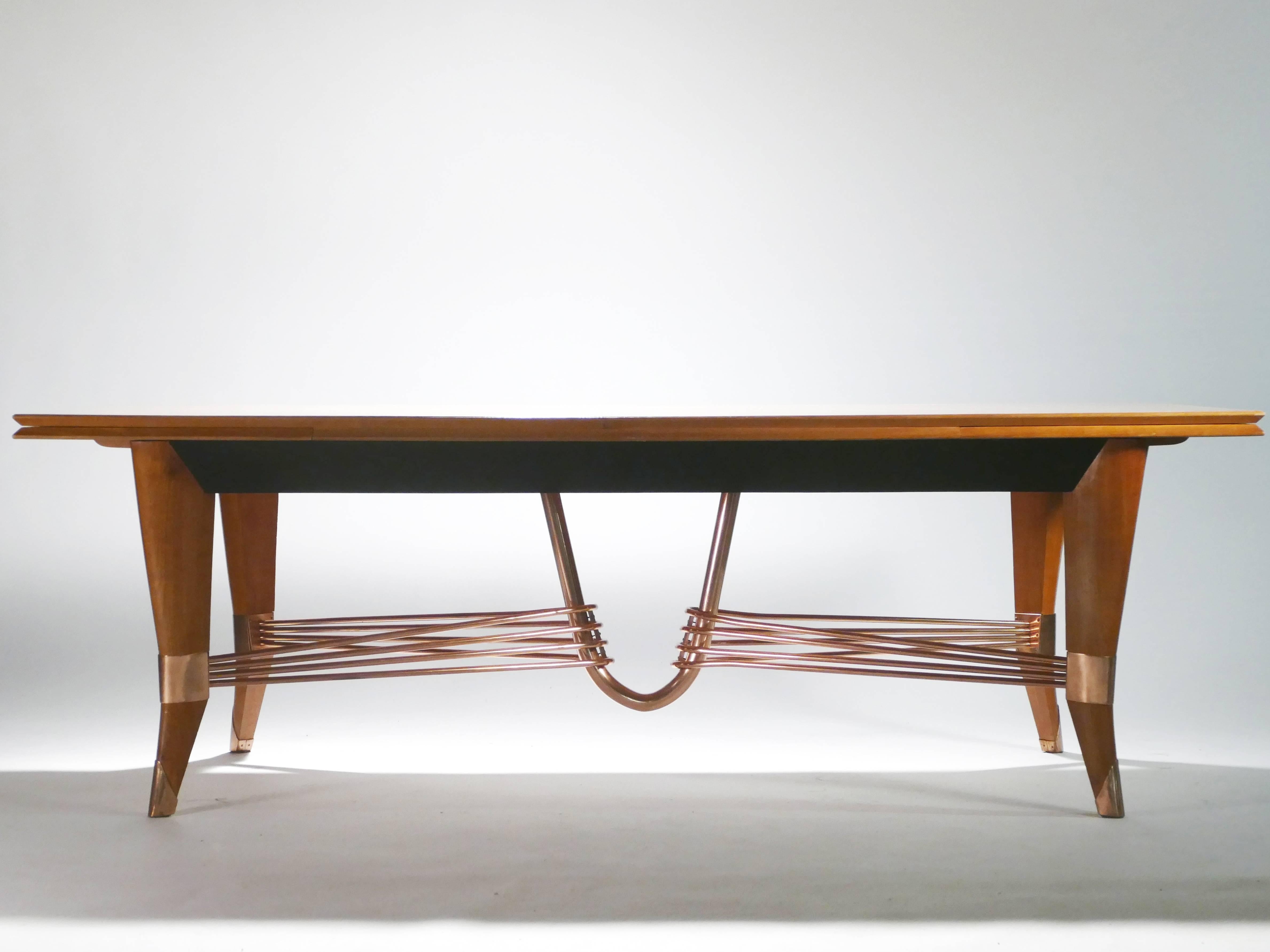 Strong, beautiful copper appears almost elastic as it’s suspended between each foot of this large dining table. The table’s immense, oak-wood varnished top is sleek and warm, providing an ideal, functional surface, while the inventive copper