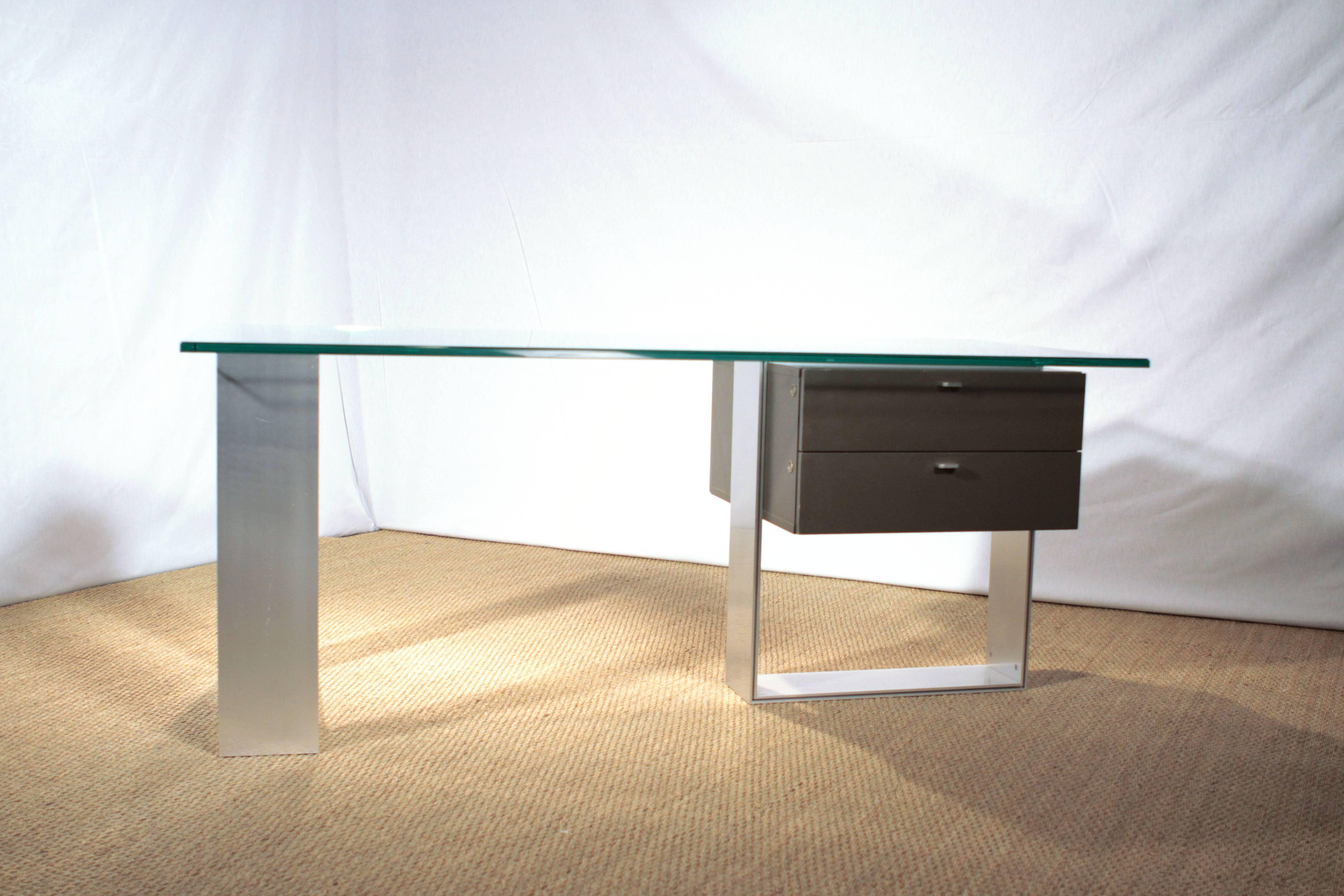 This modern office desk which published by Behr International in the early 1960s, has strong architectural lines in its design. It comes with a top in 2 cm transparent tempered glass, stainless steel metal base and a matt lacquered wooden drawer.