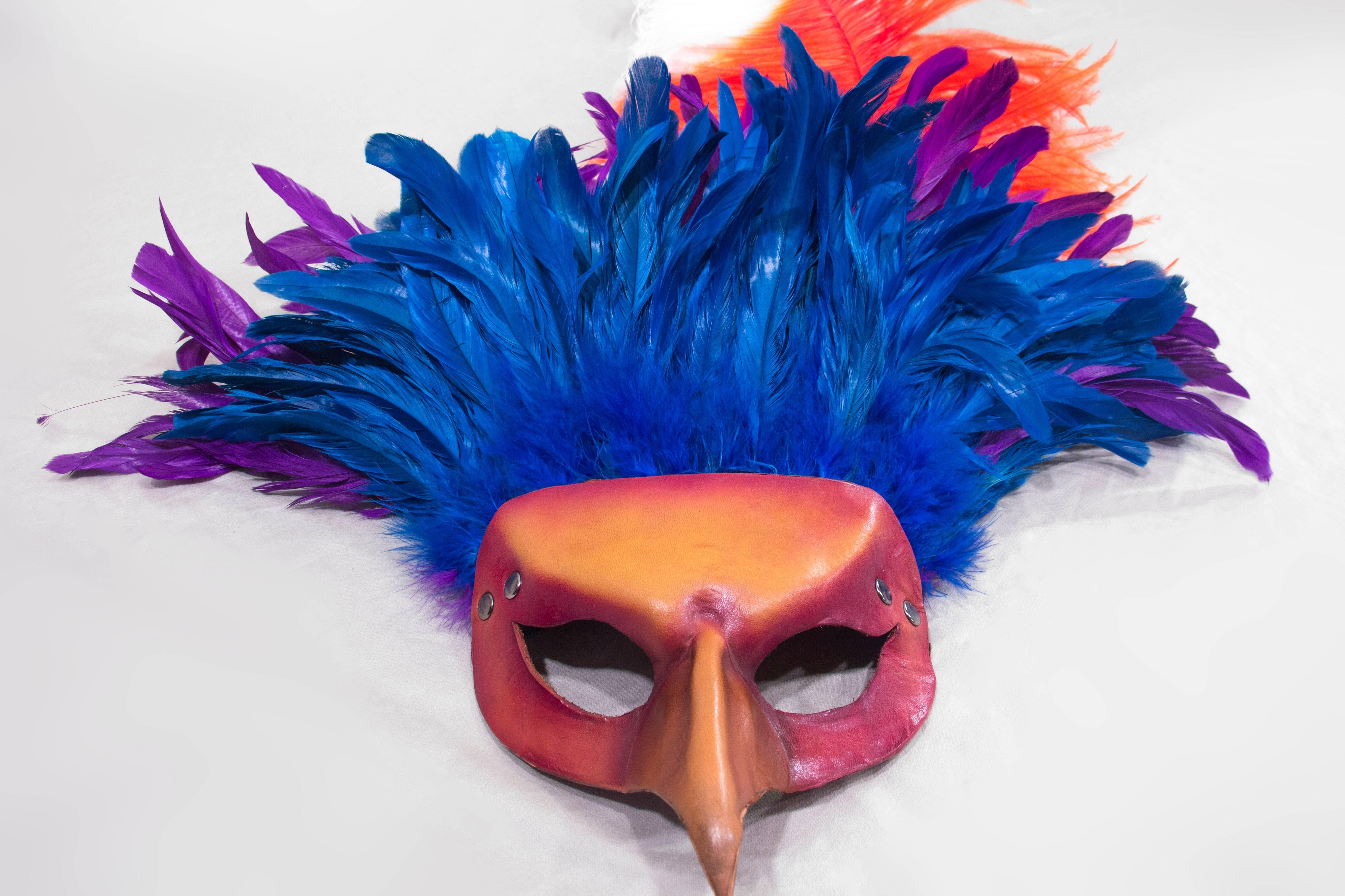 Inspired by Mardi Gras and Venetian masks. Vibrantly dyed blue and purple feathers crown this purple and yellow bird with a large orange dyed ostrich feather with a white tip to really stand out at any party or parade. This piece is wearable art,