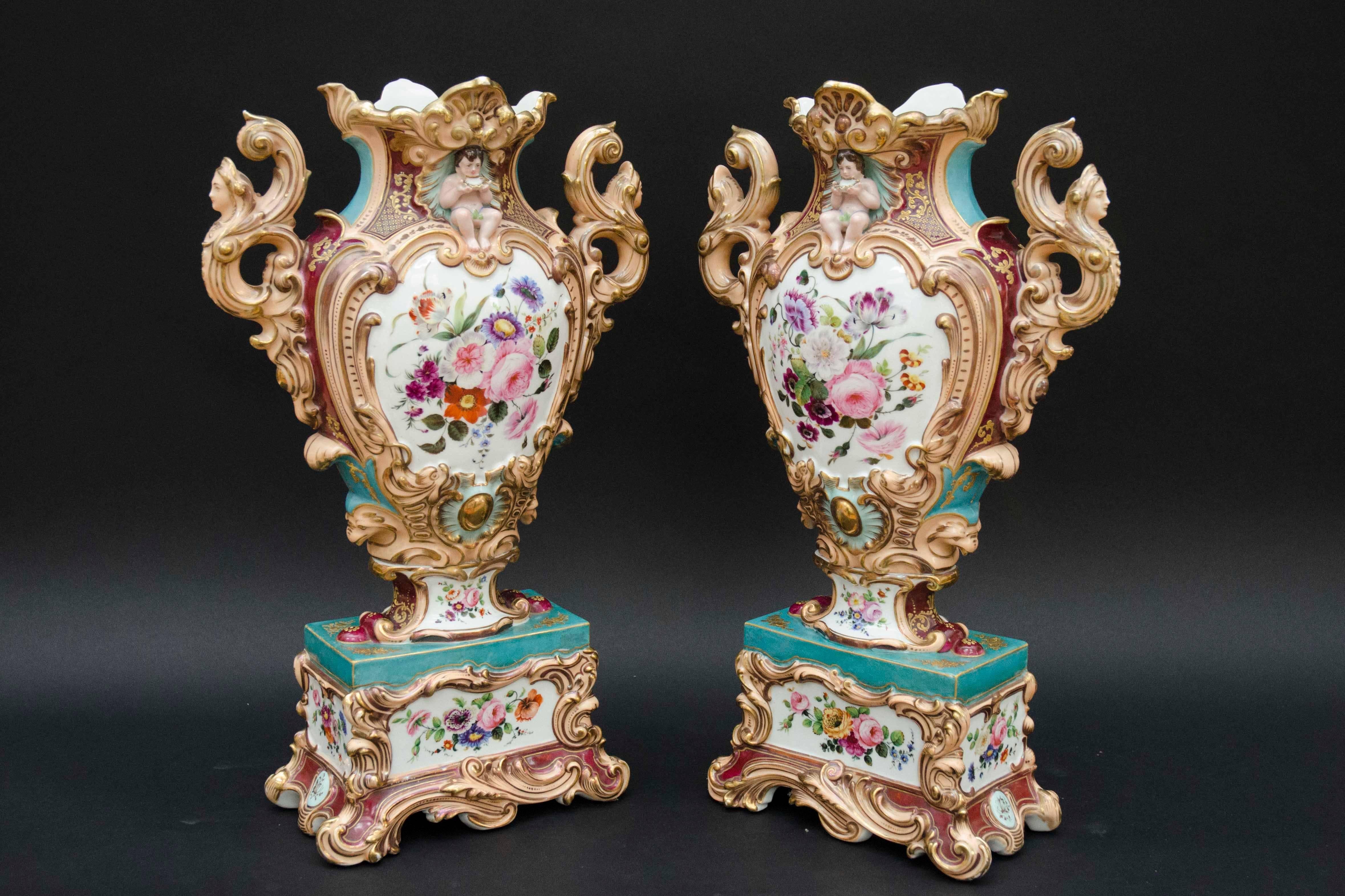 Large pair of very decorative 19th century rococo vases with flowers with colorful grounds. Handles ending in women's busts on pink ground. On top of the vases, naked children sitting in a scallop, drinking from a smaller scallop. Gilt highlights.