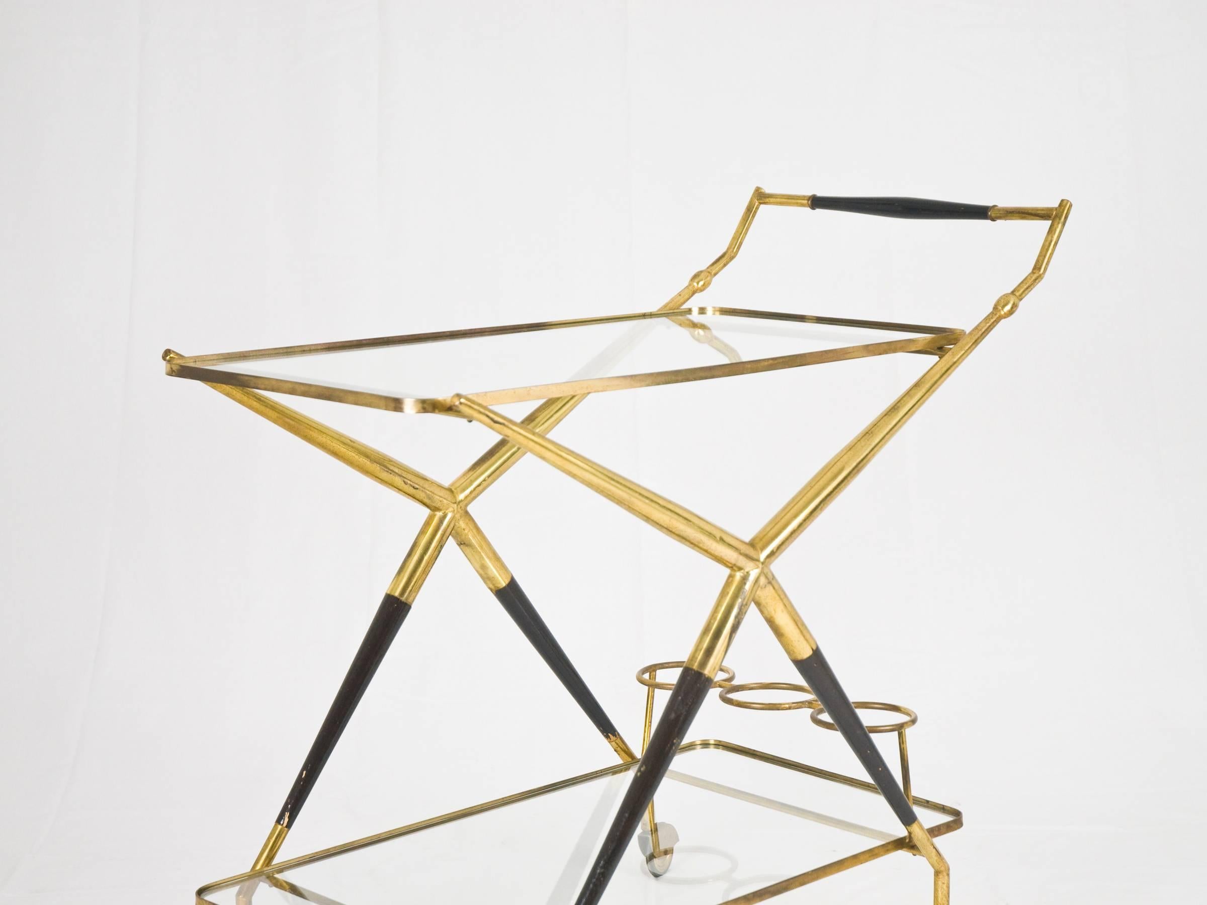This serving trolley is made from a brass and laquered wood structure, supporting two glass shelves with brass edging. All sitting on brass and rubber wheels.