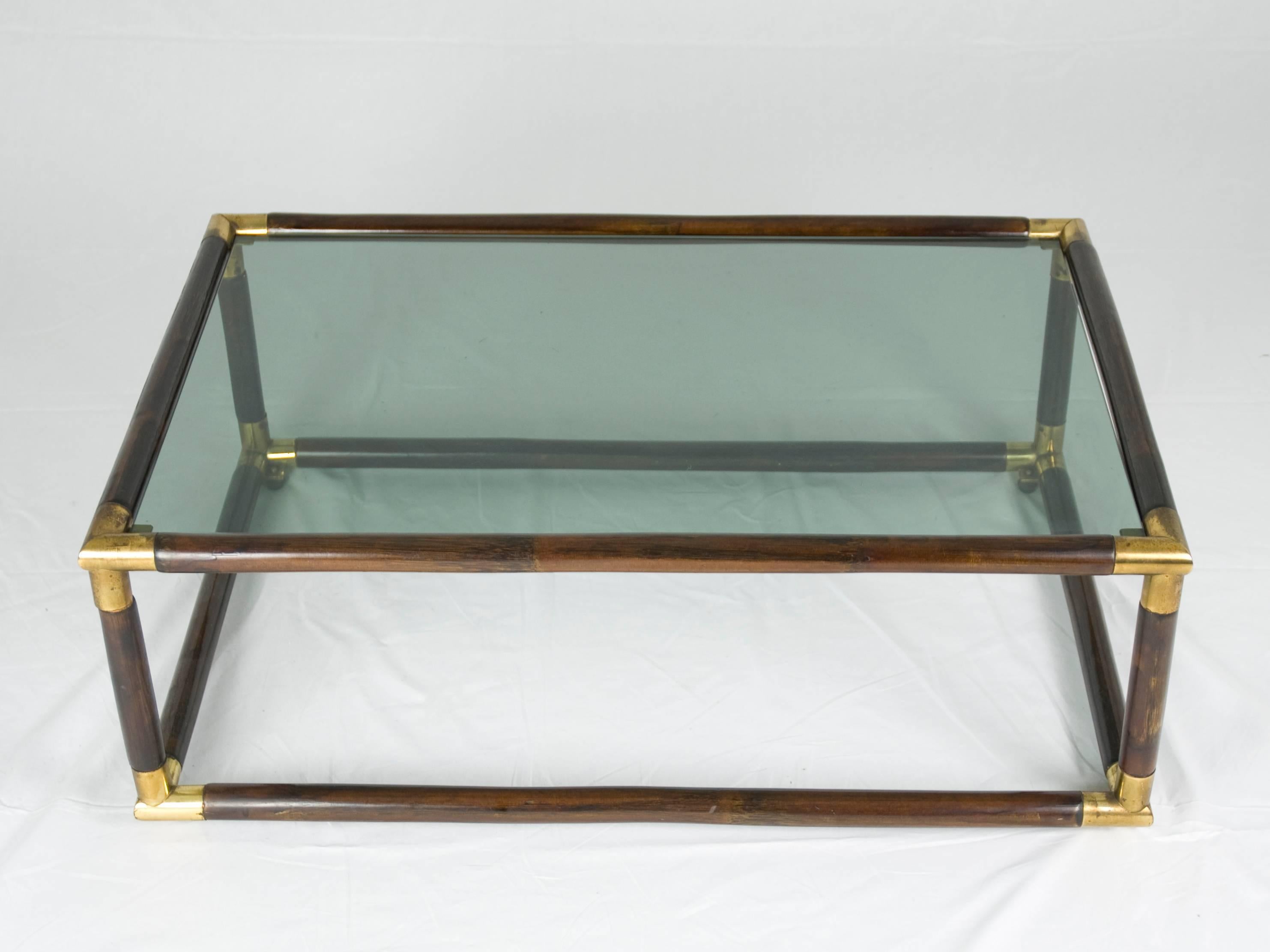 This elegant coffee table was produced in Italy around the 1970s. It is made from a laquered bamboo structure with brass junctions and features one smoked glass shelf.
The table remains in excellent vintage condition: a small chip on the edge of