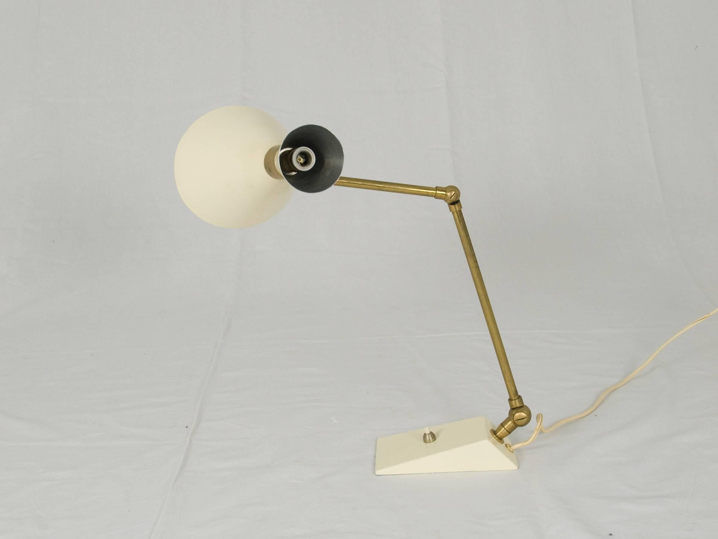 This articulated table lamp was designed in Italy in 1950. It is made from matt brass and painted metal. The biconic shade has two bulbs. The paint has been renewed.