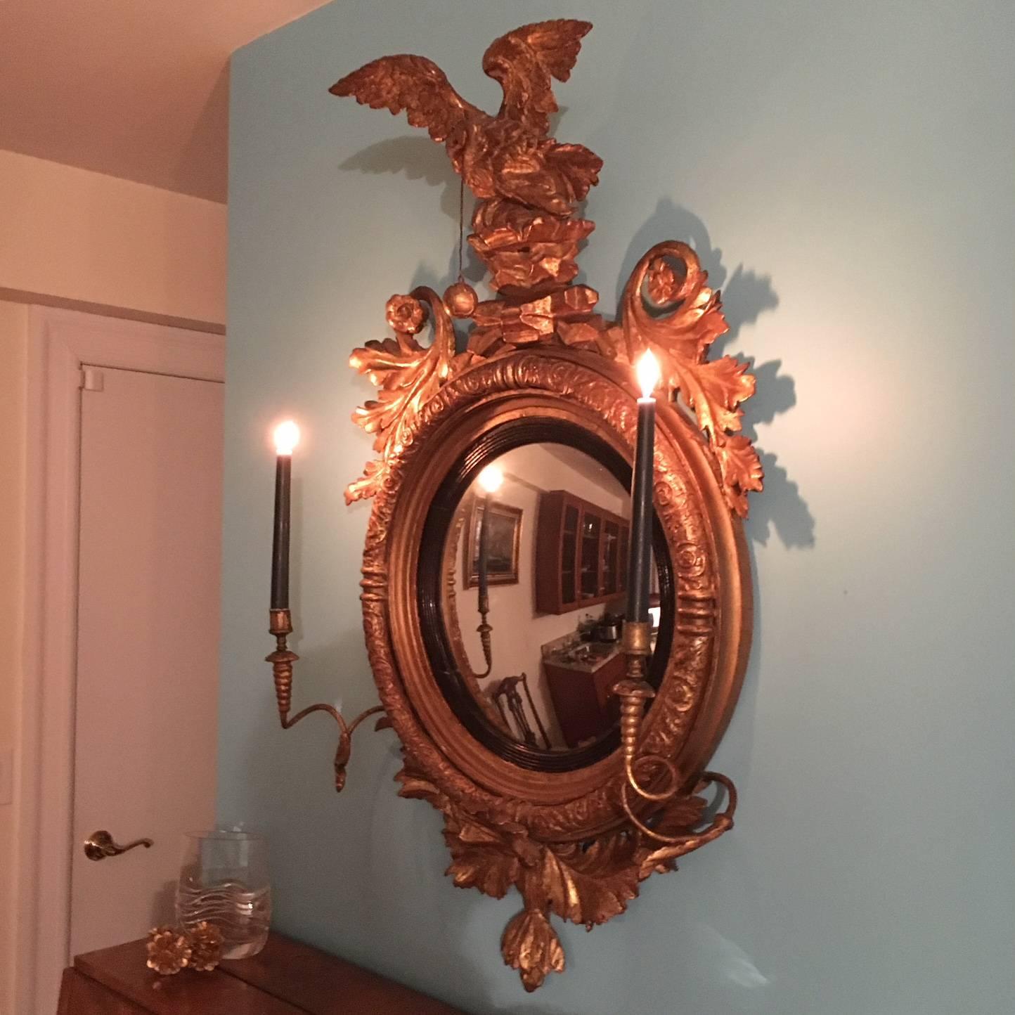 Glorious late 18th or early 19th century giltwood and gesso girandole Regency (possibly Federal) mirror, with convex mirror framed by ebonized reed and two candle brackets. Beautiful carved frame. This exquisite round wall mirror is topped with a