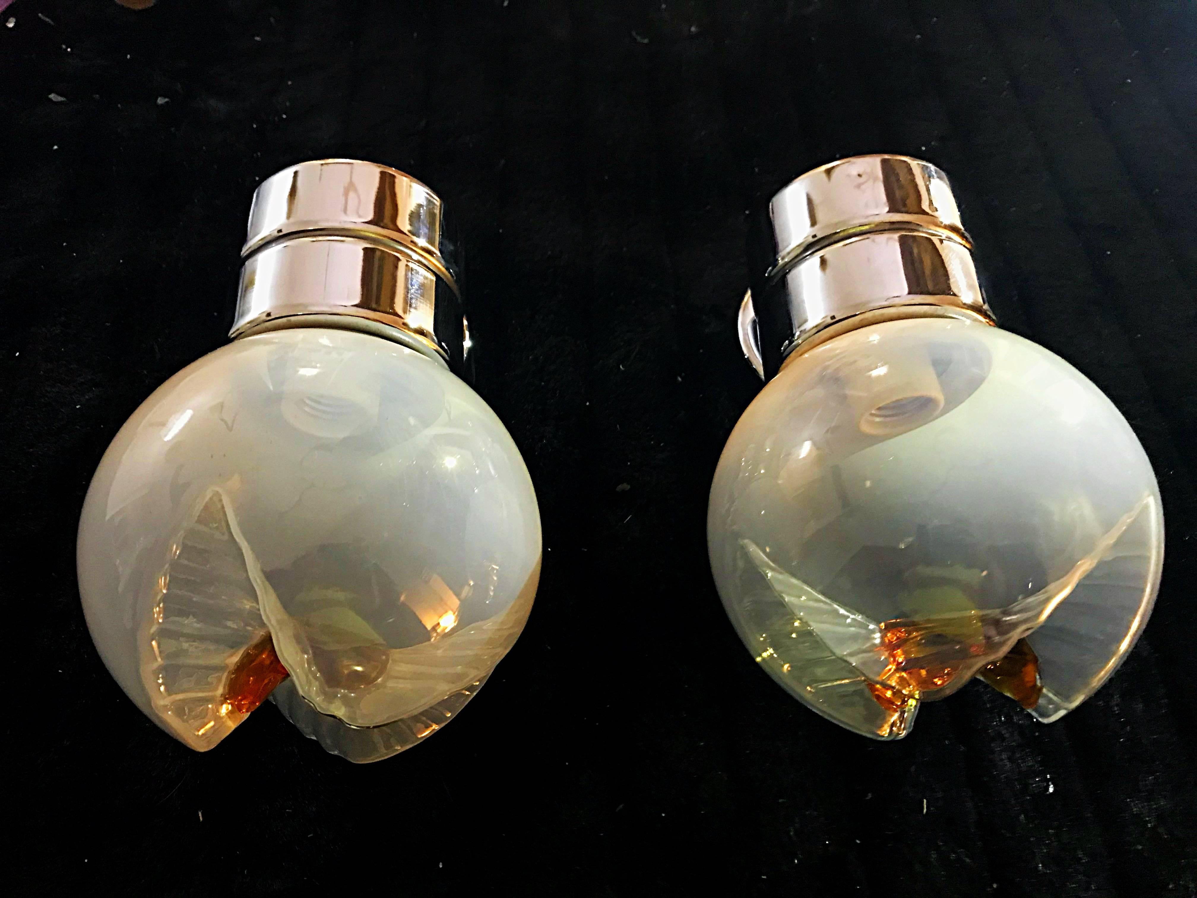 An appealing pair of Italian wall sconces, circa 1960s, by Mazzega. Each sconce has a colorful art glass shade in the form of a globe with amber coloring. The sconces have elegant sculptural chrome elements make the support of the Murano glass