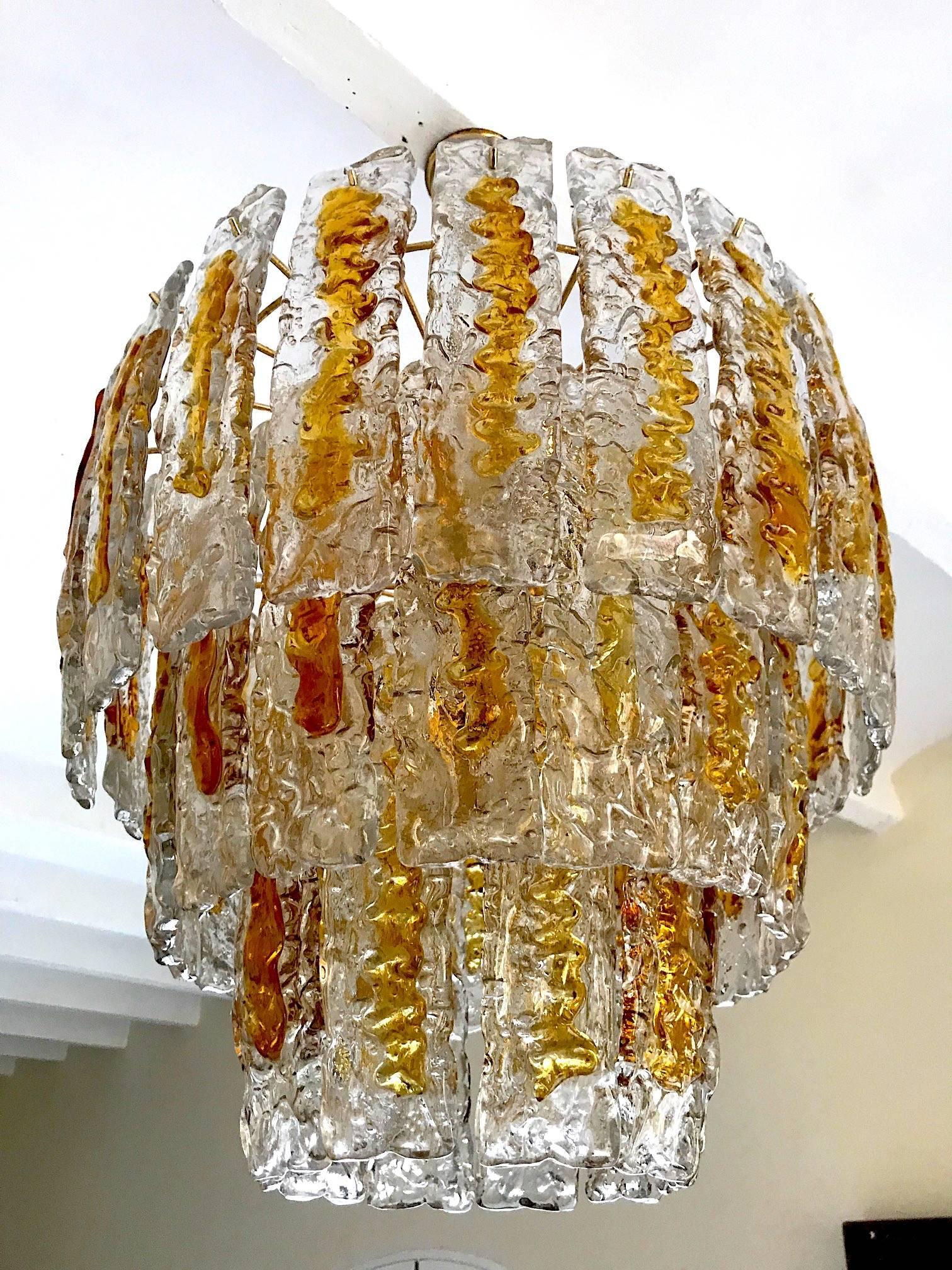 Italian Mid-Century Modern amber colored glass chandelier handblown in Murano by Mazzega. This Piece has a double layer of glass and imparts a warm light. The inner layer has ten pieces and the outer layer has 49 long pieces with both forming an