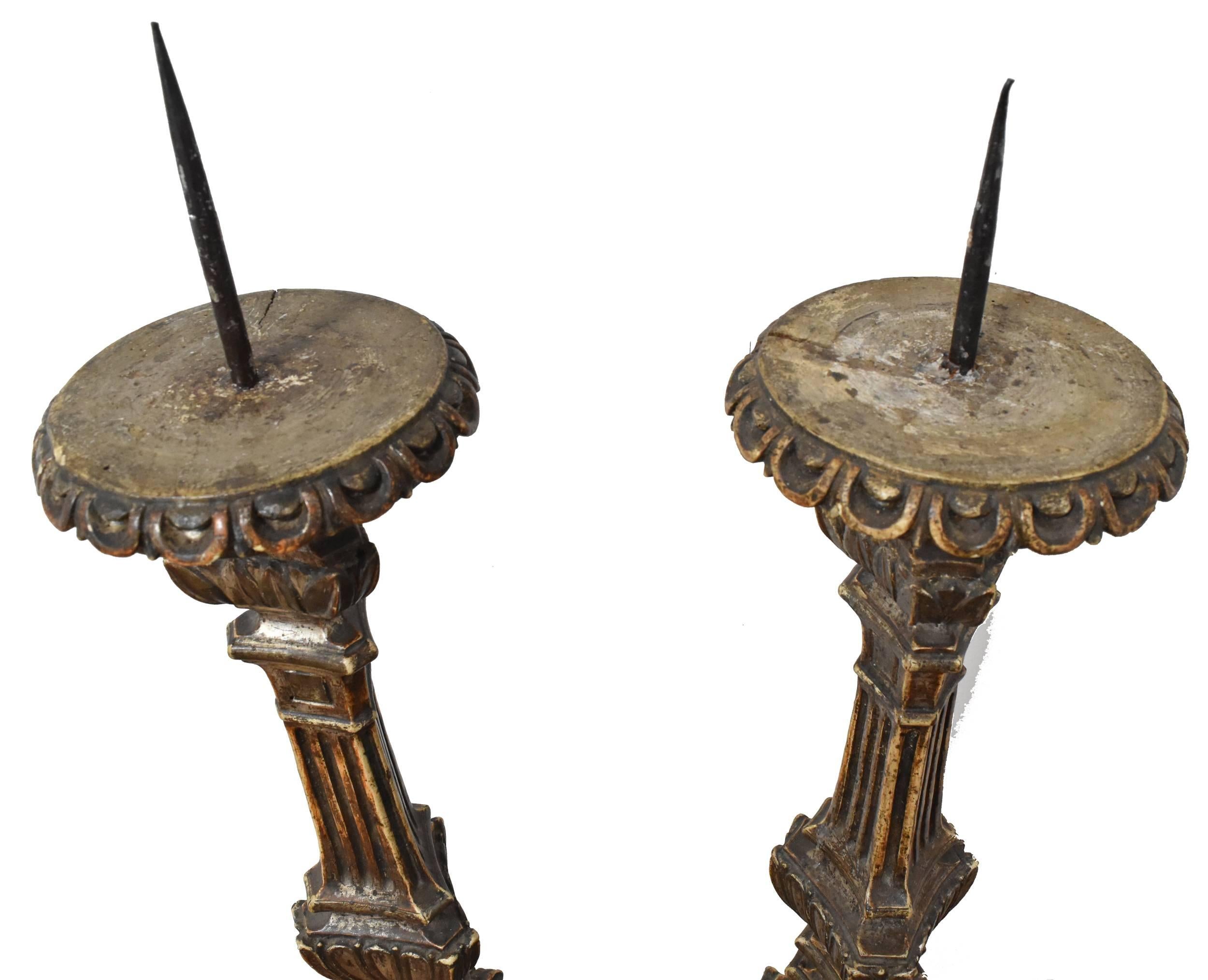 Pair of tall carved wood altar candlesticks with elegant ornamental details gilded in silver, topped with period iron prickets to hold large candles. 

 