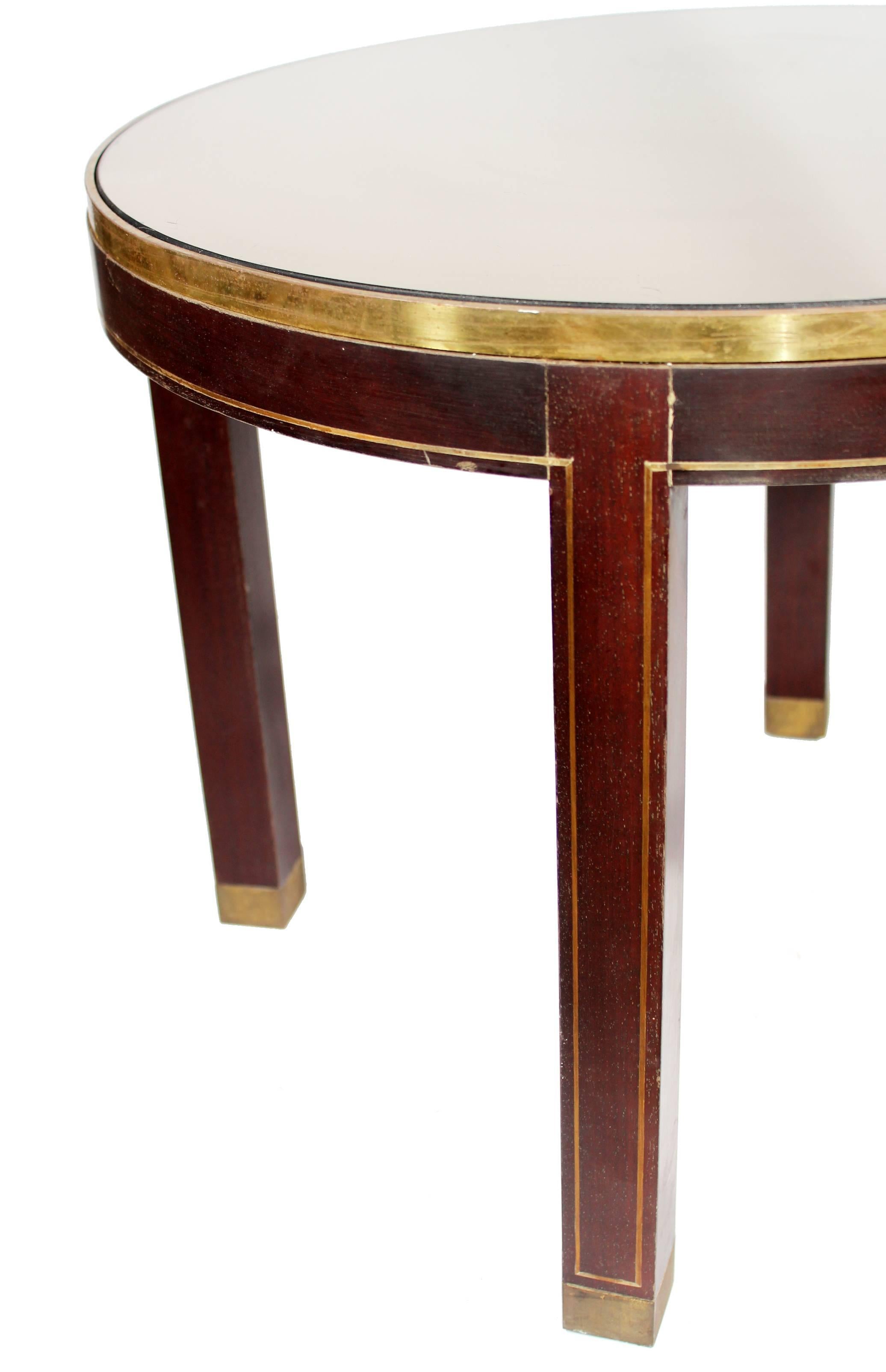 Spanish pair of round side tables with a thin strip of brass framing the mahogany wood rim and brass tipped legs. Original smoked mirror tabletop, which in the photos is reflecting a white ceiling.