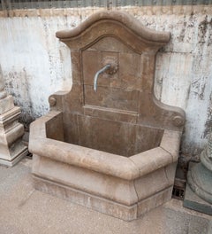 Fuente de pared de piedra natural con cuenco y caño decorativo.