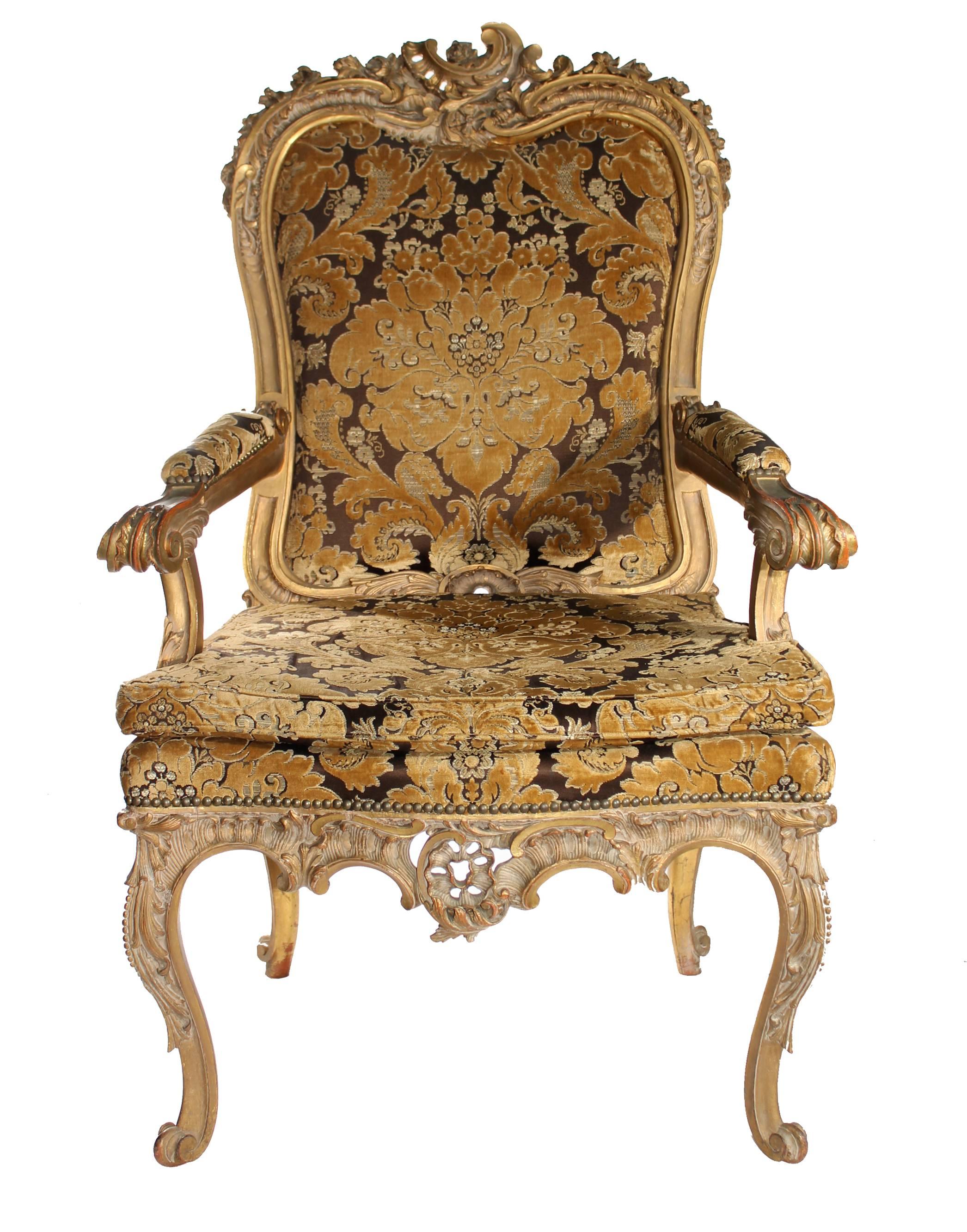 Fauteuil en bois fruitier de style baroque français, sculpté à la main, avec des décorations de rochers et de plantes typiquement néoclassiques, dorées à la feuille d'or et peintes dans d'autres couleurs. Tapissé de velours à motifs floraux dorés et