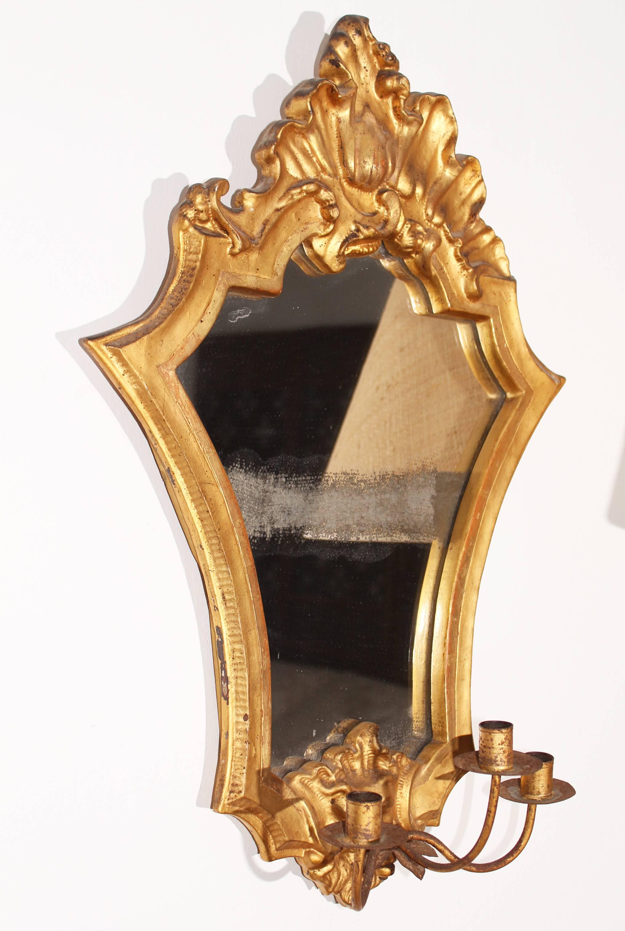 Pair of 18th century gold guiltwood mirrors and iron scounces with late Baroque Rococo broken shell motifs atop, and a bass-relief carved face below. 


 