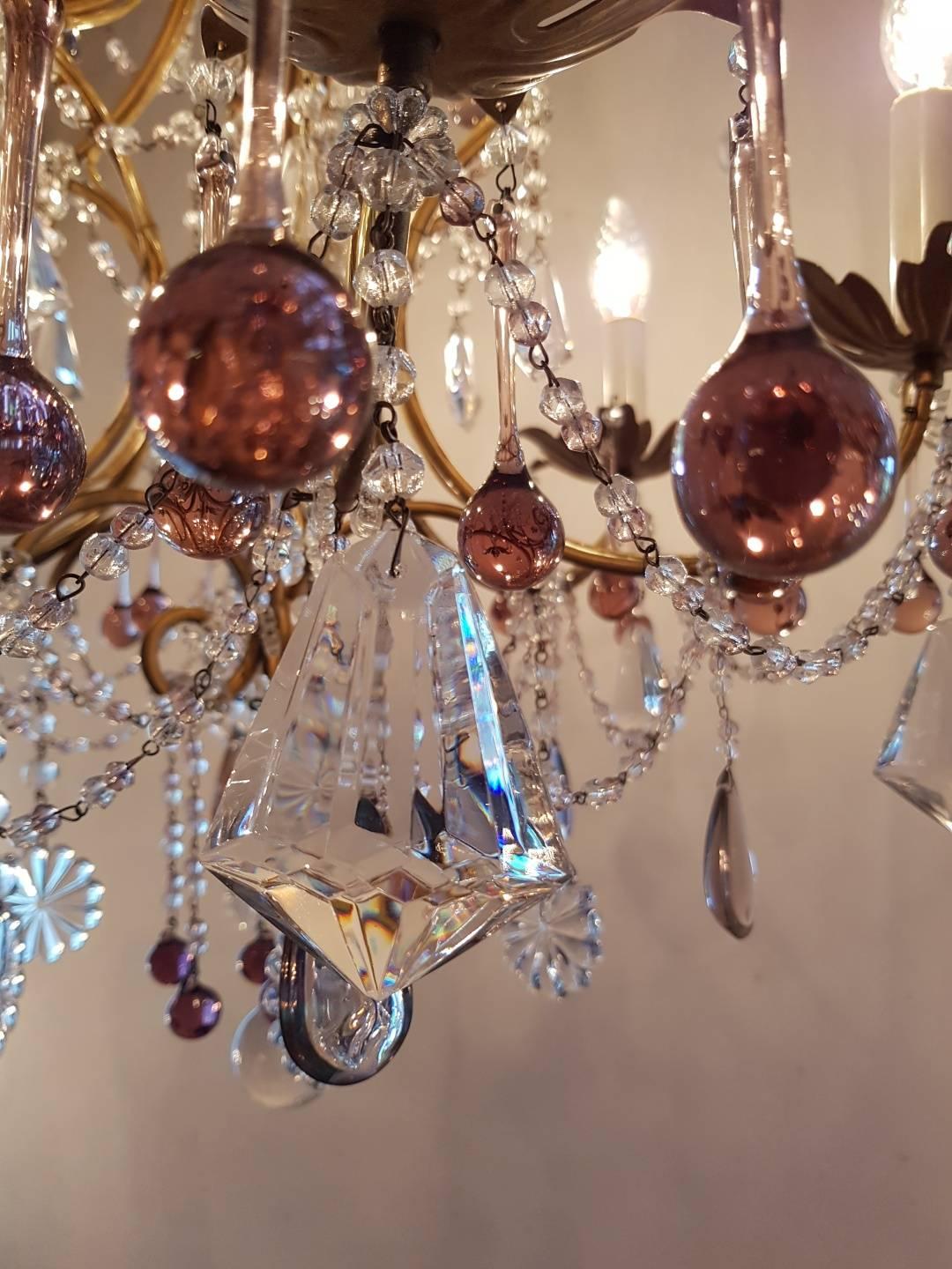 Small, delicate Italian chandelier with nice colored drops and small strings of crystals in pink. Six-light. Iron frame in brass color.
This is just one of the collection of 1000 chandeliers, ceiling lamps and wall lightning. Our collection is very