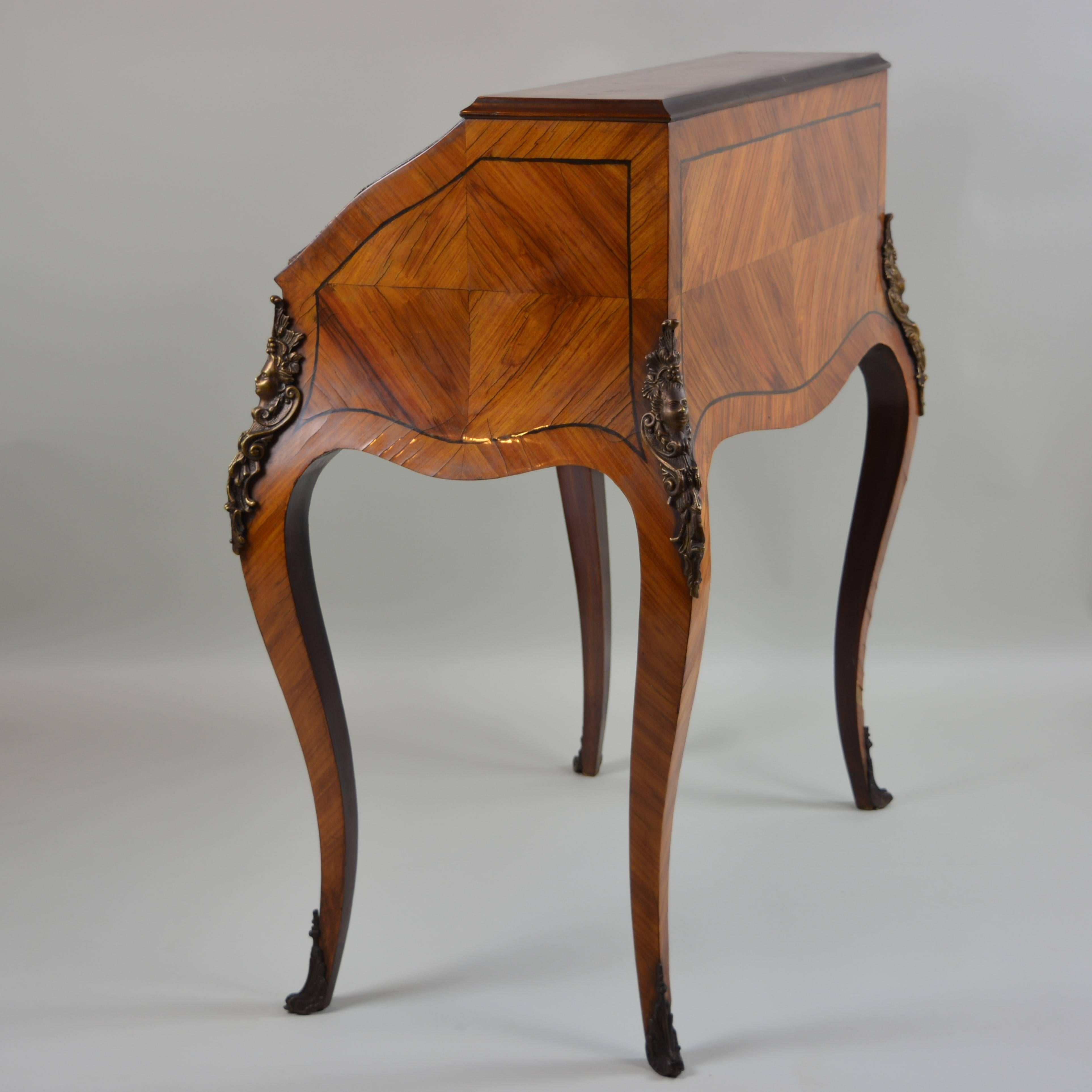 Beautiful flowing curves and rich veneers make this elegant little desk exceptionally pleasing to the eye. With fancifully curved legs and plentiful brass adornments, it hides its functional features well: the full-width front storage drawer, the