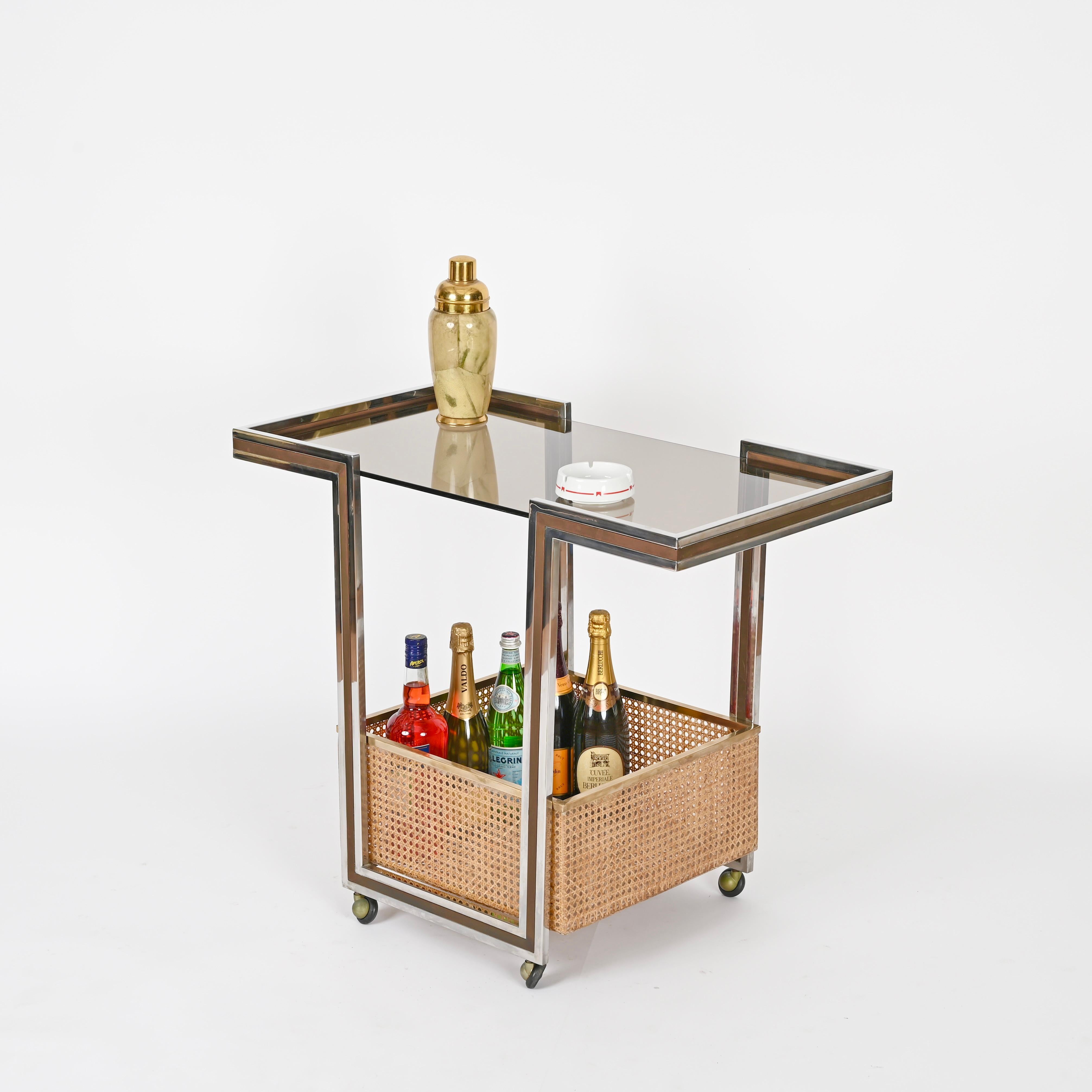 Exceptional and unique Italian serving bar cart in chrome and brass with an incredibly stylish bottom tray in lucite and Vienna straw and completed by its original smoked glass top. 
This marvelous piece was designed by Willy Rizzo and produced in