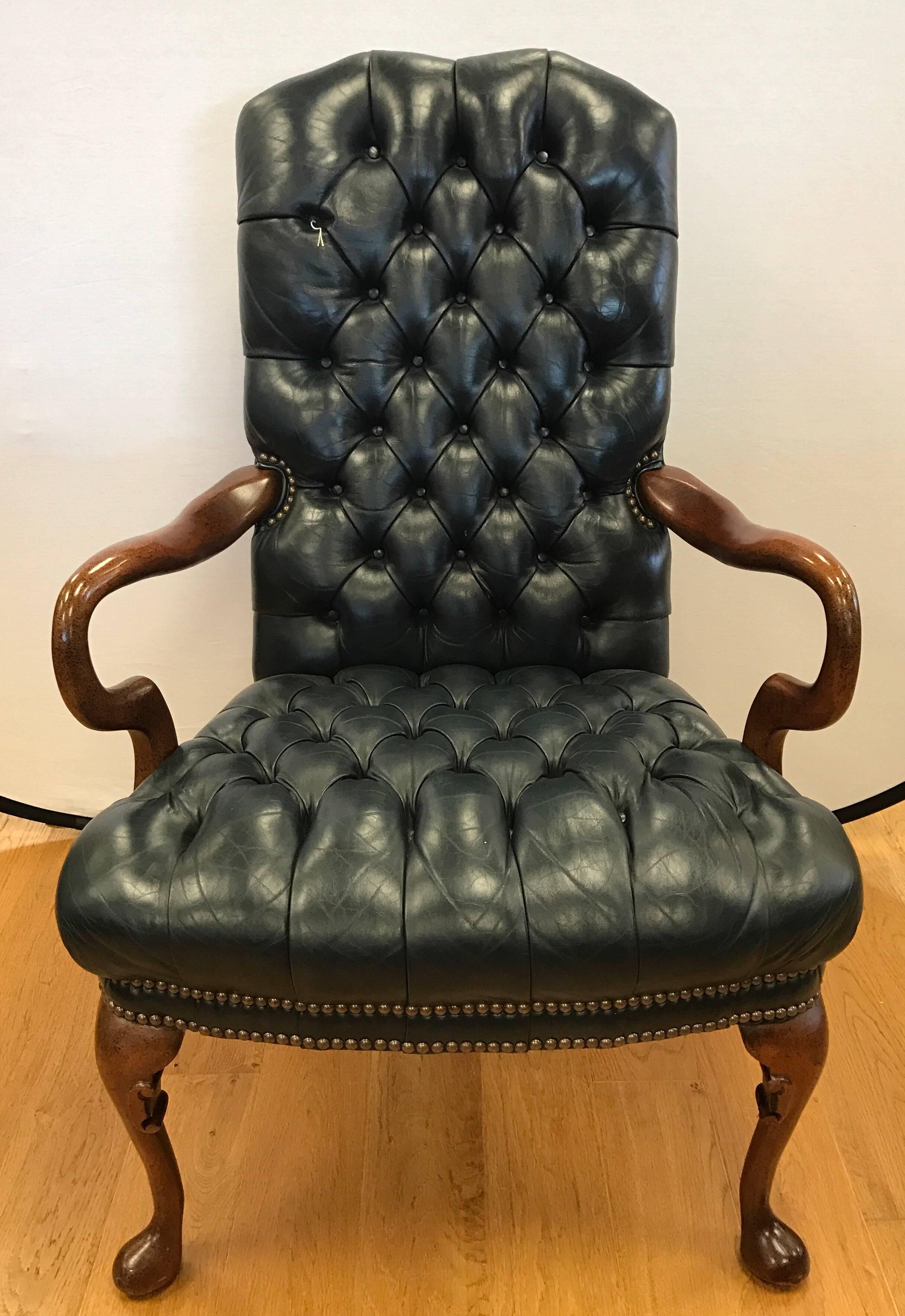 Pair of leather armchairs featuring Classic Chesterfield style tufted seating surface upholstered in a rich navy leather with brass nailhead trim accents.