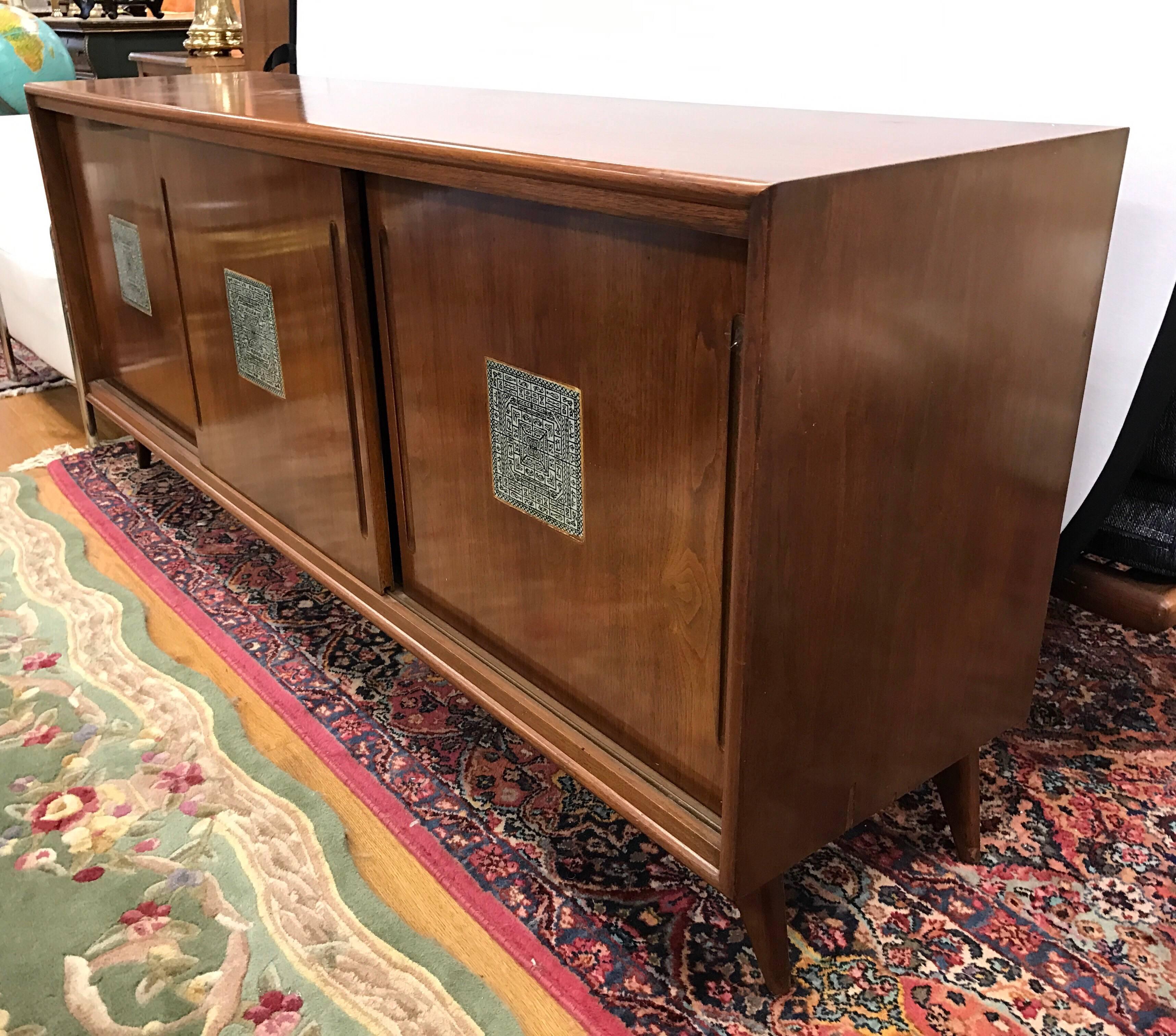 Midcentury walnut sideboard credenza with three sliding doors with tile inserts. The left and center compartments have three drawers; right compartment has two inserts for glasses and bottles.