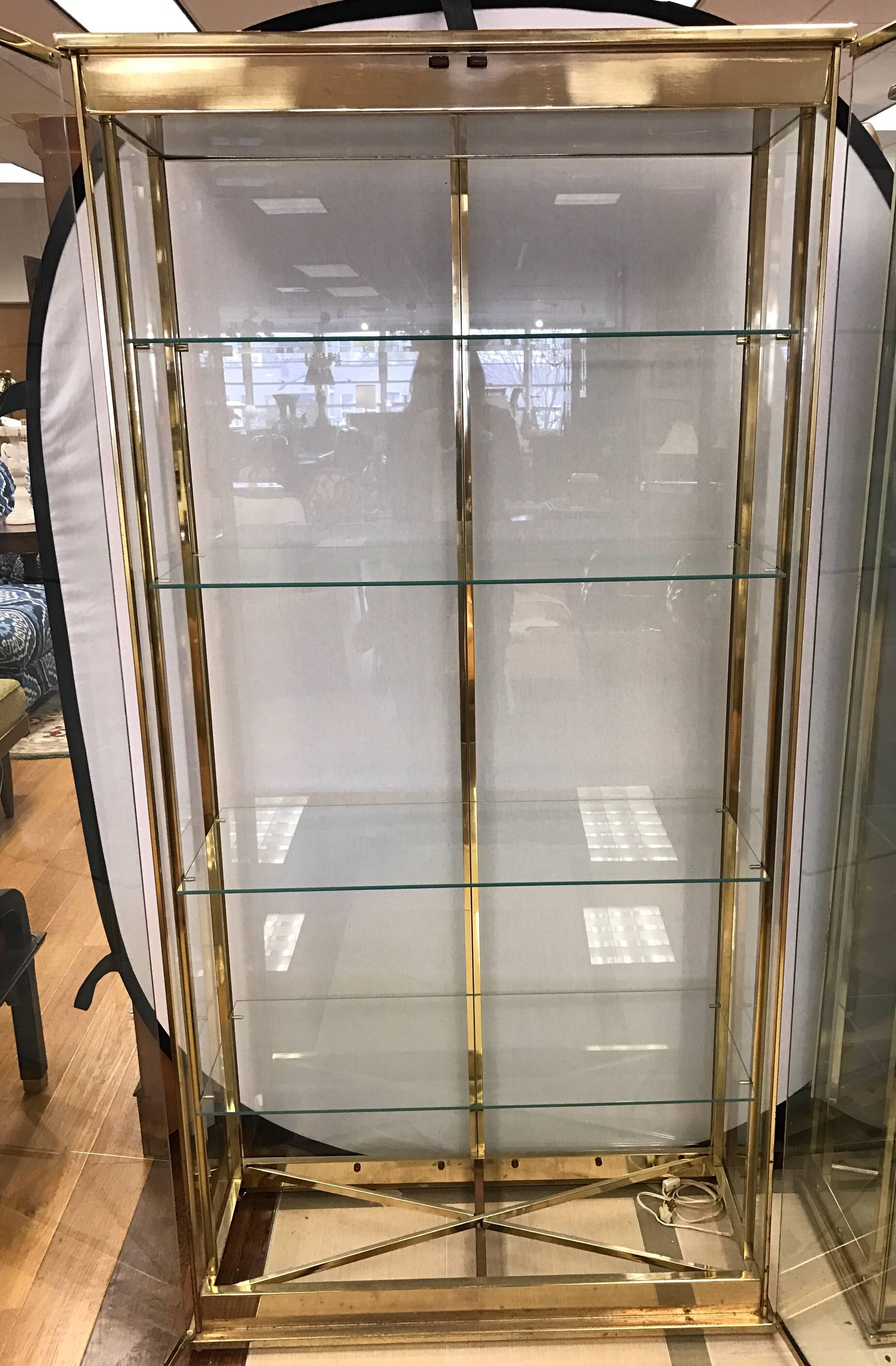 Pair of midcentury brass and glass Mastercraft vitrines with four glass shelves. These cabinets are electrified and are lit from above.