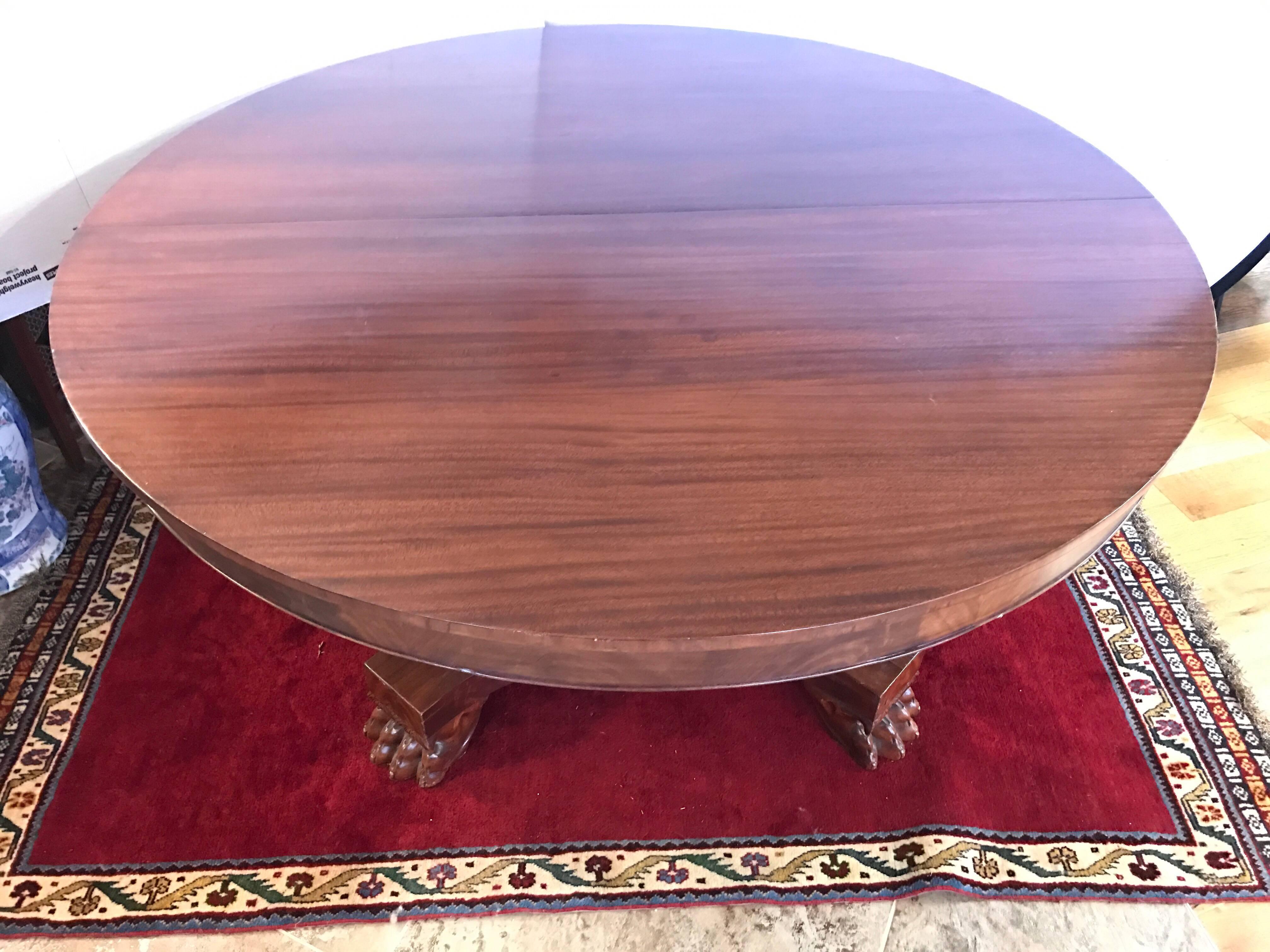 Magnificent antique English mahogany round dining table supported on a four-sided substantial pedestal column base terminating in four carved lion paws. No leaves.