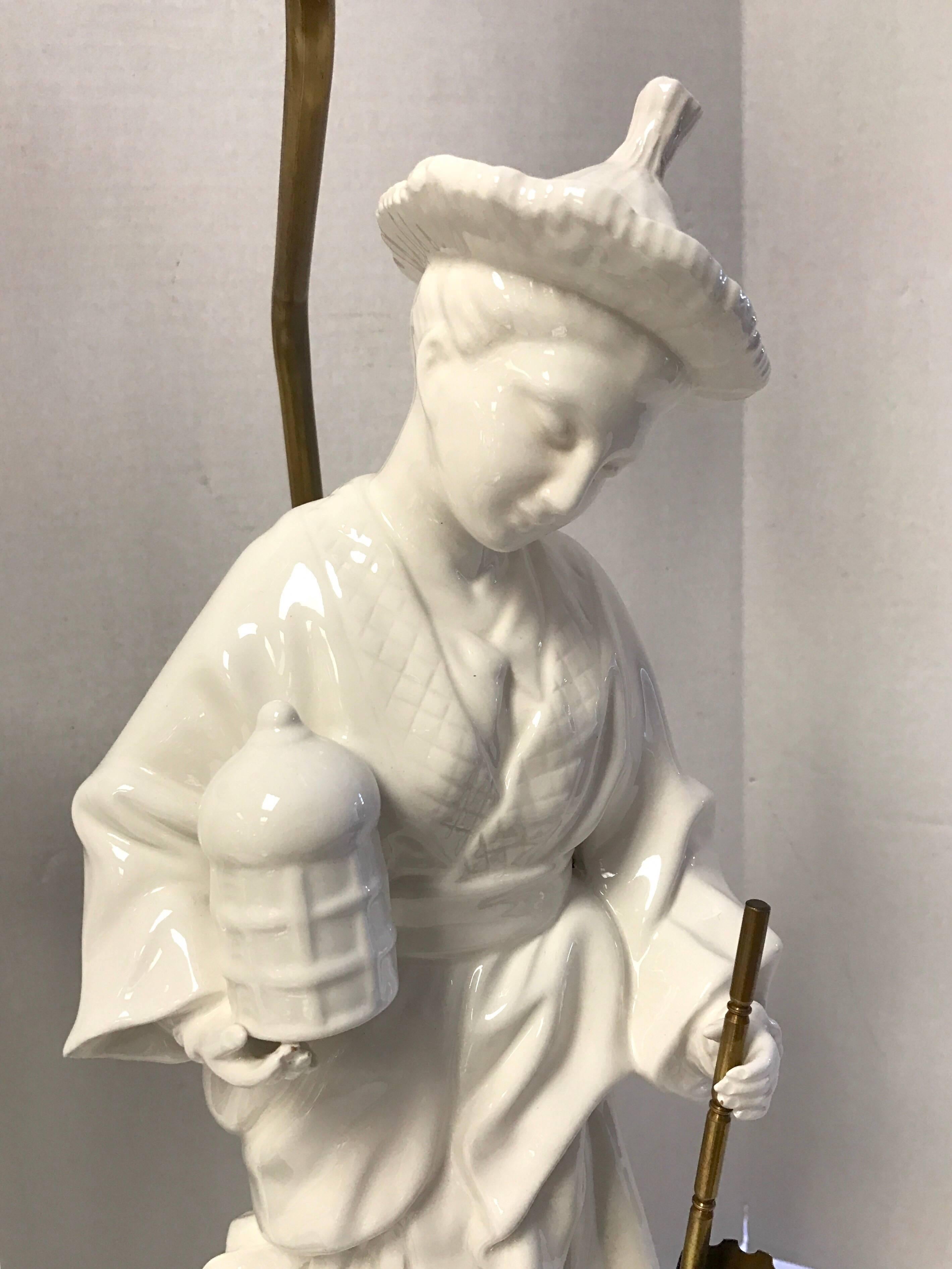 Pair of blanc de chine porcelain figural lamps mounted on wood bases. Male figure holds a brass umbrella. Female figures holds a brass closed umbrella. Lampshade is pleated paper and is included. Overall height 33 inches; 16 inches to top of socket.