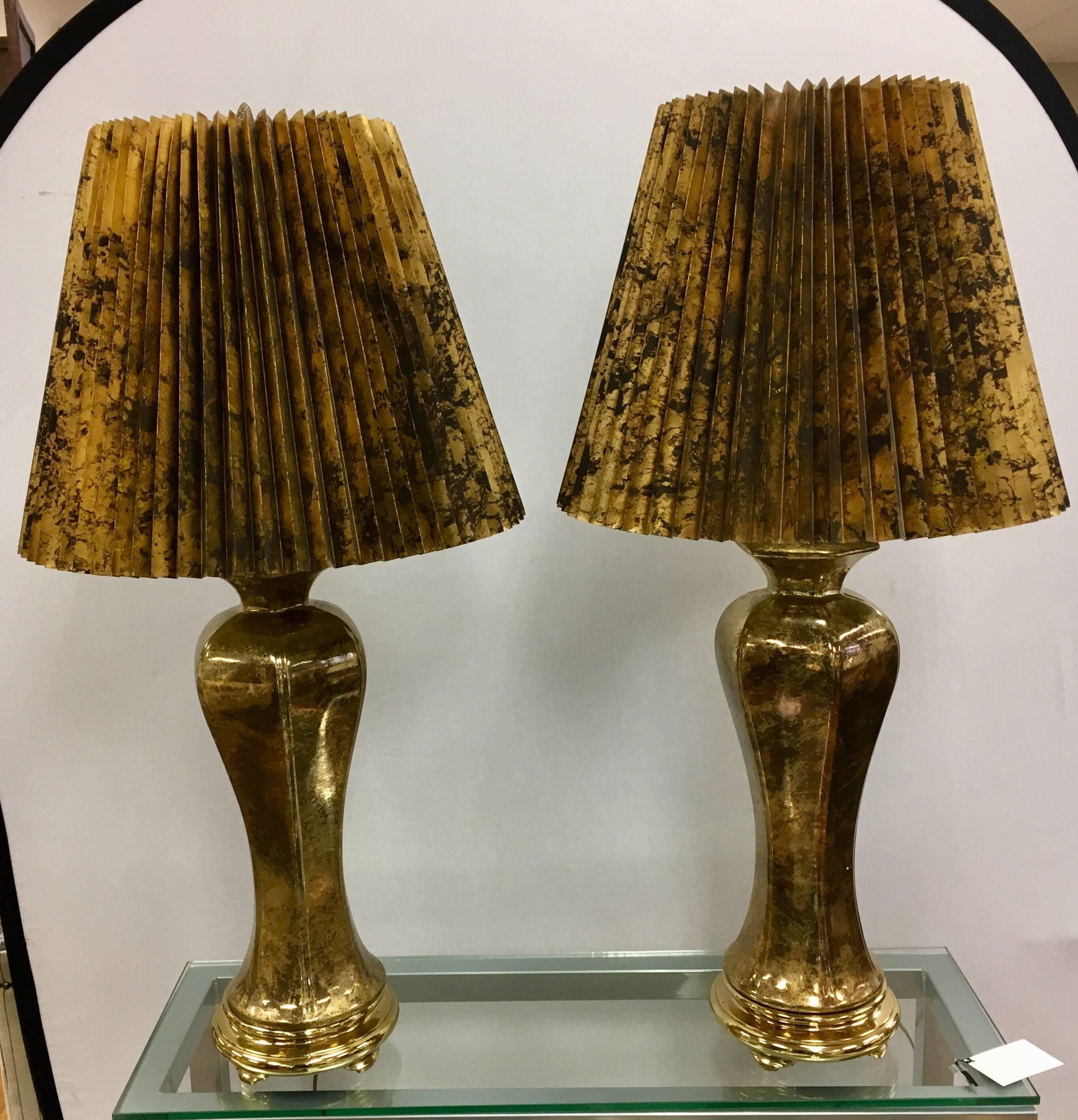 Coveted pair of Hollywood Regency urn shaped large table lamps glazed in gold.  They are in excellent condition and wired for US. Features include a single light socket per lamp, a shade that measures 19 inches in diameter and a brass pineapple