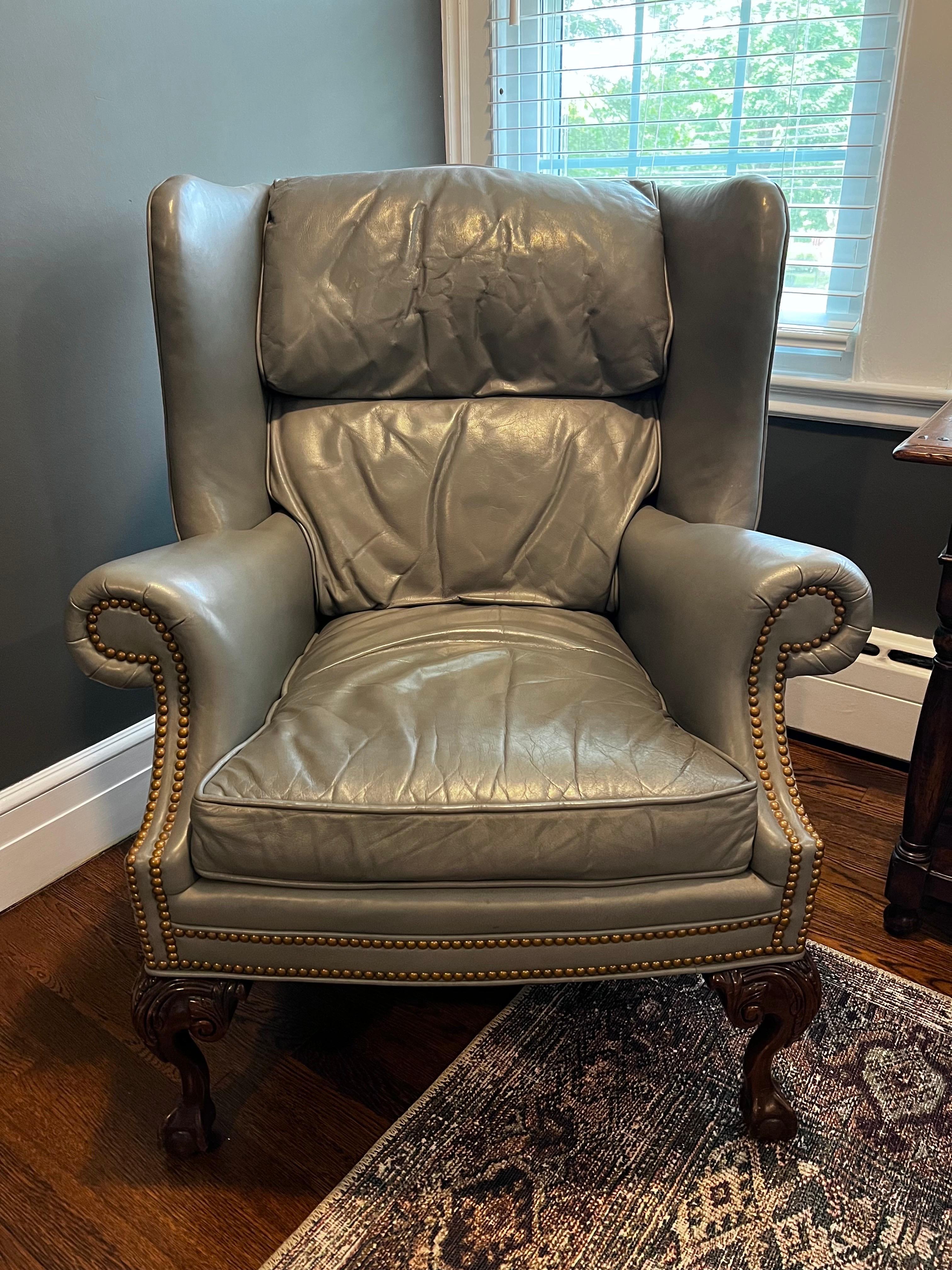 Handsome high quality gray leather wingback chair featuring mahogany ball and claw feet at front and tapered feet at back for support as well as real brass nailhead trim. Made by Farington in the USA and featuring eight way hand tied construction.