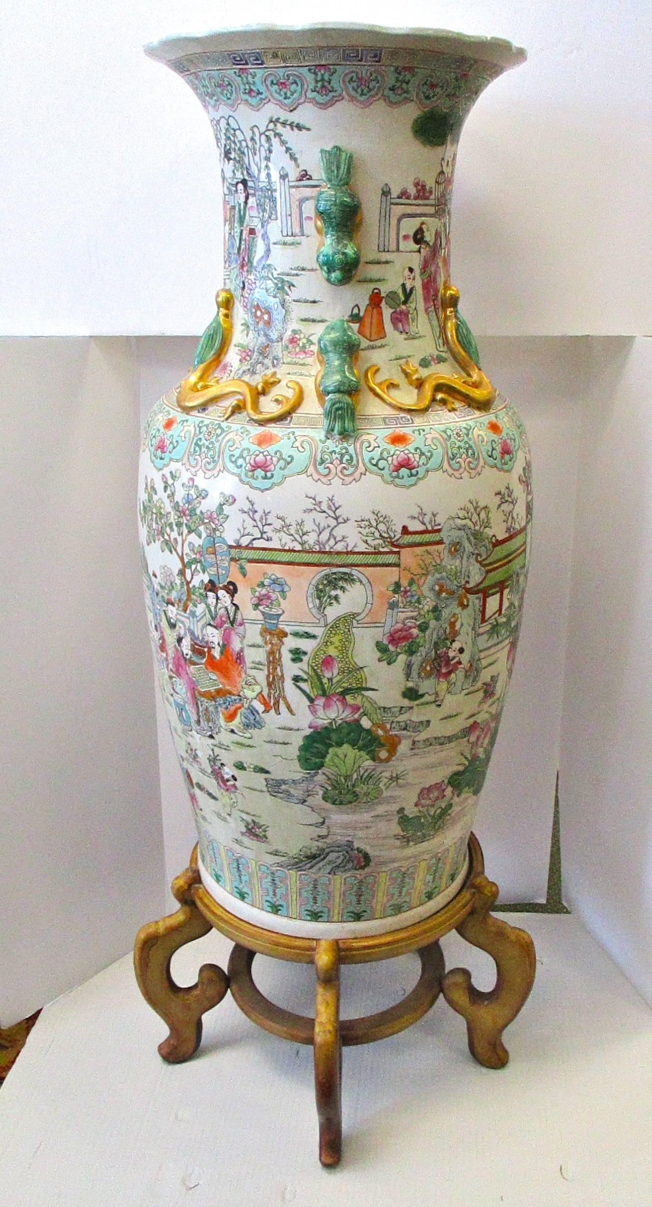 Large, 20th century palace size partially hand-painted Chinese rose medallion vase on carved wood stand with raised gilded lion dog handles and salamander detail; depicting classical Chinese scenery.
Measures: With stand, 48" tall; without