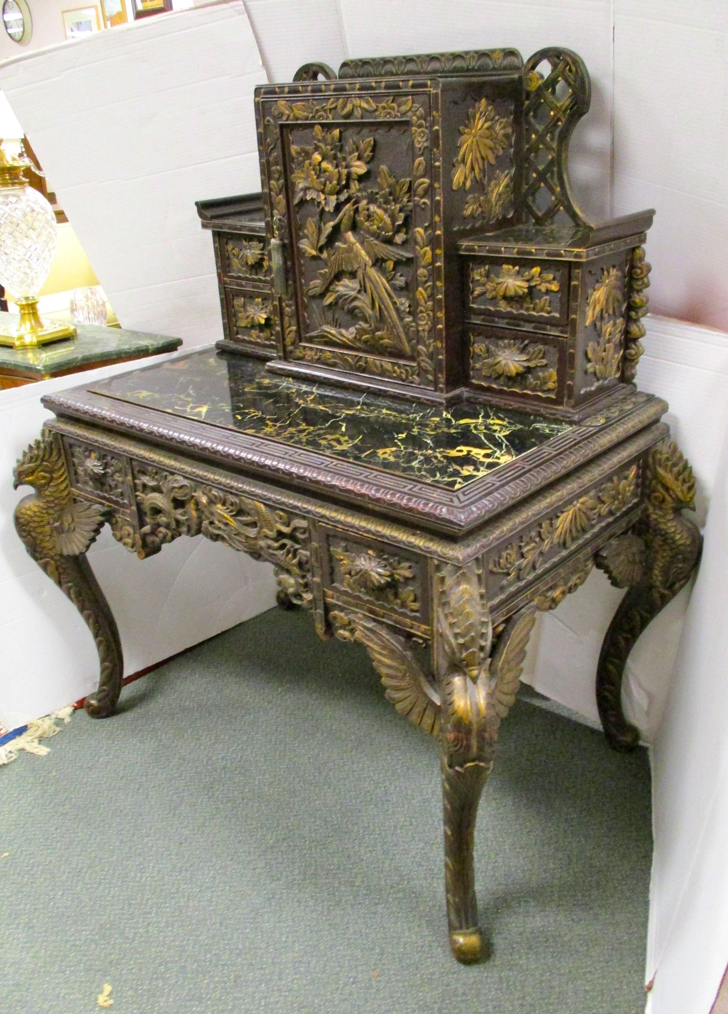 Unusual dark Chinese secretary desk, circa early 20th century, features intricately carved detail of birds and flowers with a gold finish. Carved figural birds top all four legs. Top section has four small drawers with a middle door that opens to