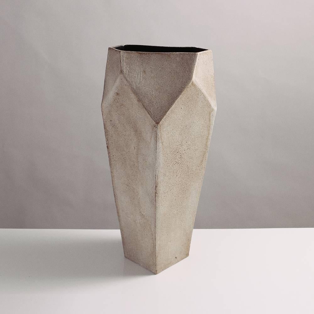 Inspired by midcentury Brutalist architecture, this tall ceramic vase combines clean geometric lines with the warmth and individuality inherent in handmade work. The shape is simple and elegant, with geometric facet detailing at the opening. Each