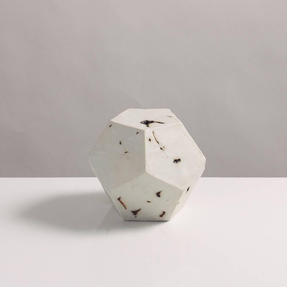 This sculptural geometric dodecahedron is handcrafted from slabs of unglazed white porcelain with highly individual black oxide burnout detailing, giving each of its 12 sides a unique textural matte finish. The organic texture contrasts with the