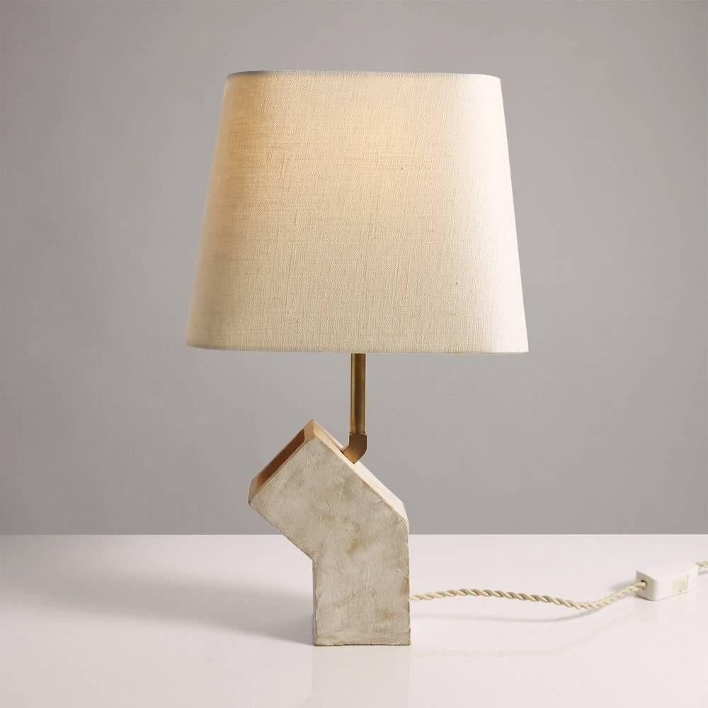 Inspired by midcentury Brutalist architecture and building materials, this small table lamp balances a strong substantial ceramic base with delicate brass hardware and a rounded geometric beige linen shade. Perfectly sized for a bedside table. The