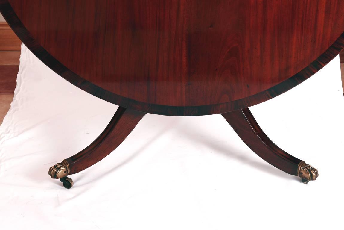 Early 19th century mahogany centre or dining table crossbanded in rosewood on a tripod base. Having original brass lion's paw castors. The top can be tilted to the vertical for easy storage when not in use.