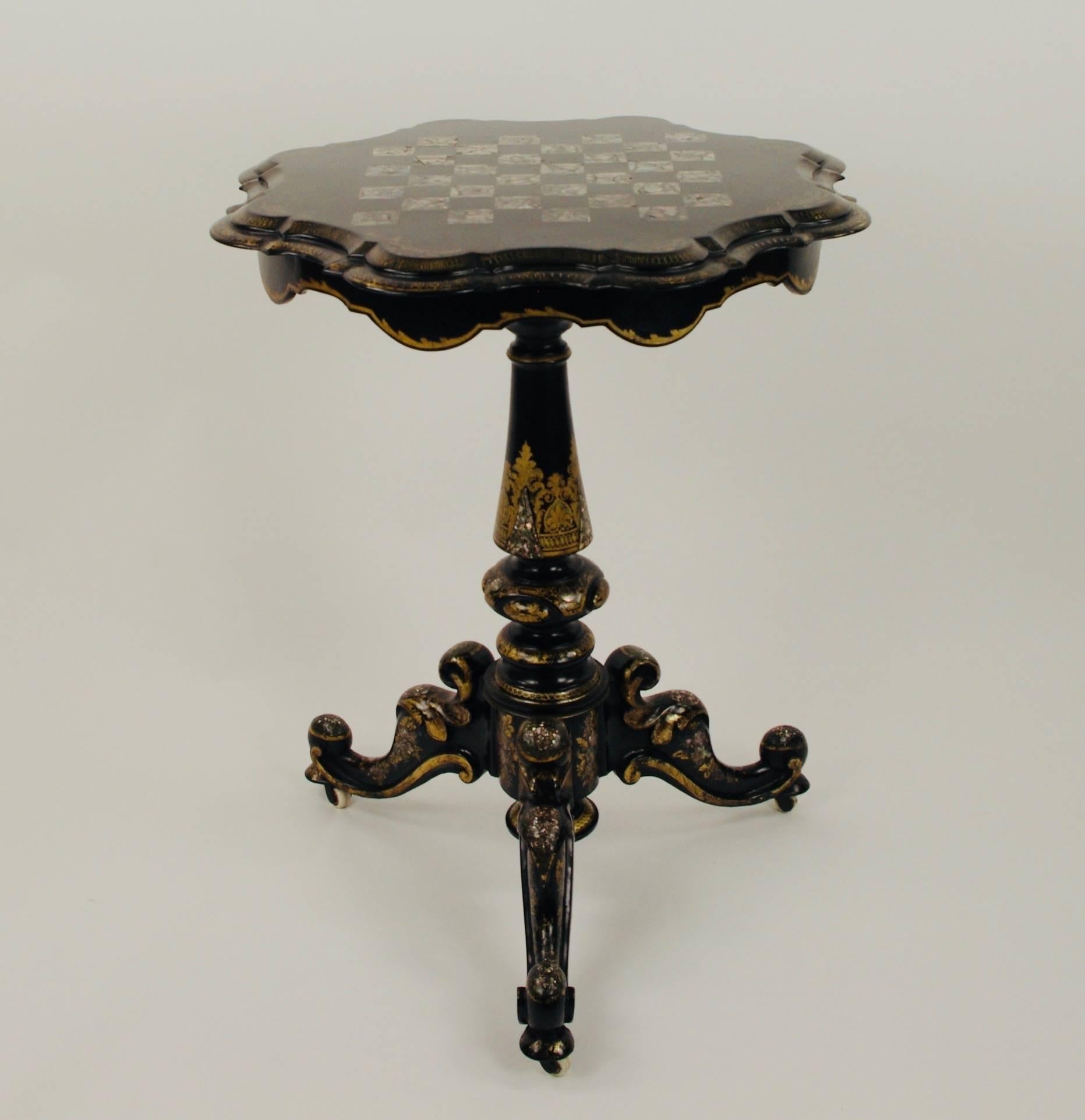 Japanned gilt lacquered tilt top games table, the cartouche shaped top inlaid with a mother-of-pearl chequer board on tripod scroll base.

This item is on show in Berkshire UK