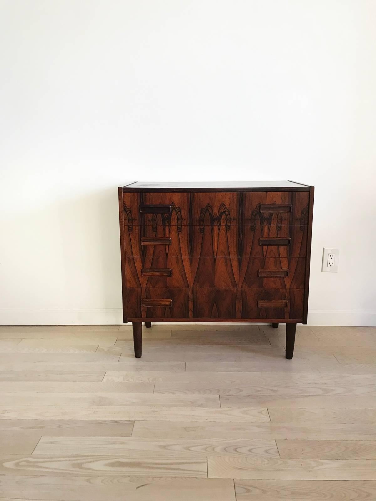 Beautiful grain and bookmatched rosewood on this midcentury Danish chest of drawers. Four drawers, peg legs and rosewood pulls. Classic Danish design in a stunning vibrate rosewood. Water mark ring on top back left corner, pictured. Drawers pull